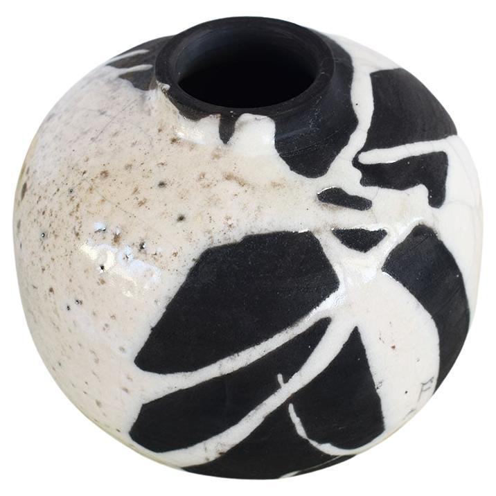 This vase is a beautiful example of studio pottery. It is round and created from ceramic. It has a black matte background, with white craquelure glaze applied in a marble design. A small opening at the top with slightly fluted edges is perfect for