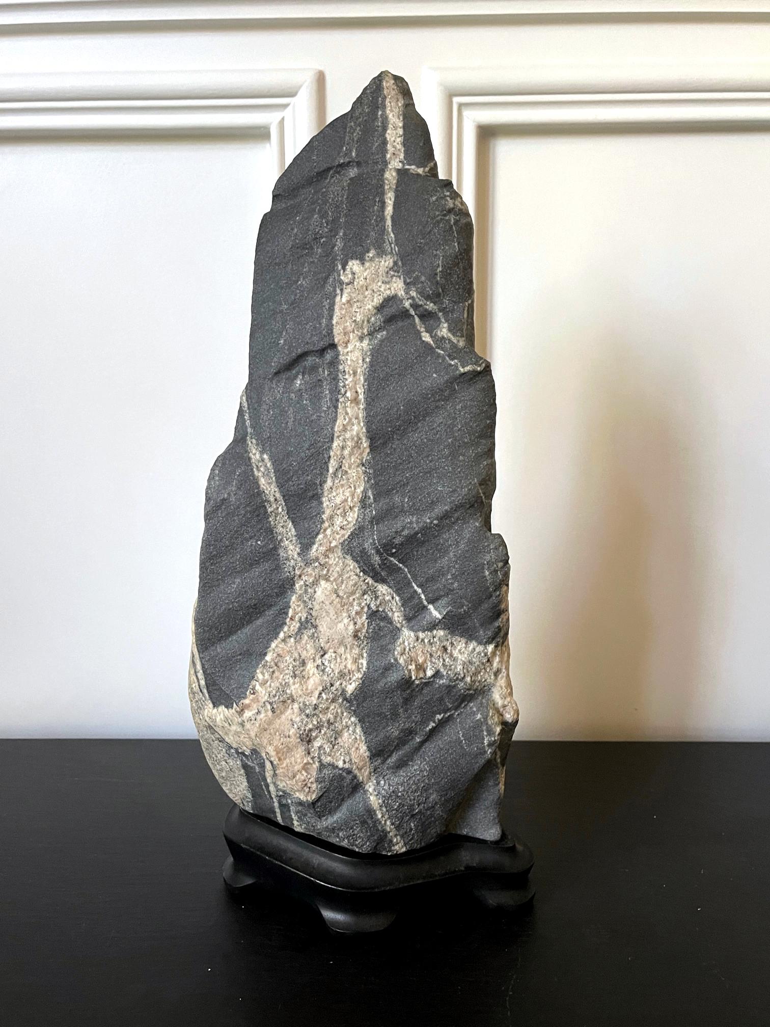 On offer is a large and expressive scholar rock on a fitted wood stand collected by an American collector in Palm Desert, CA circa 1980s. The deep grey boulder is likely granite and takes a wonderful natural form of a mountain peak. The dark matrix
