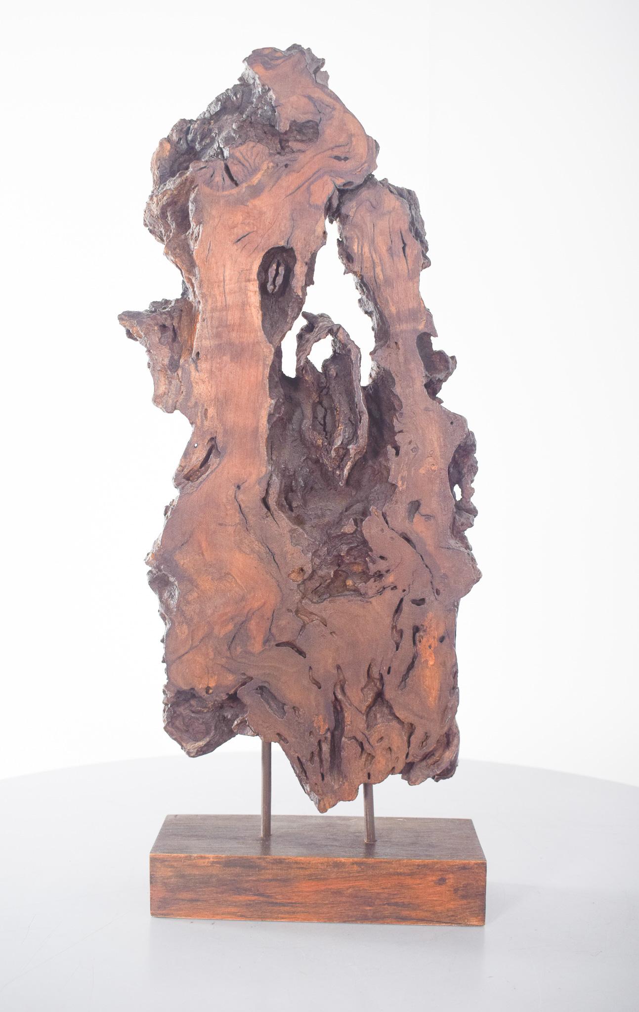 Scultura astratta in legno di noce. Il frammento per la scultura è stato ricavato da una radice di tronco invecchiata, montata su una base di legno con due discreti supporti metallici per conferirle stabilità e aumentarne la verticalità. 
Il design