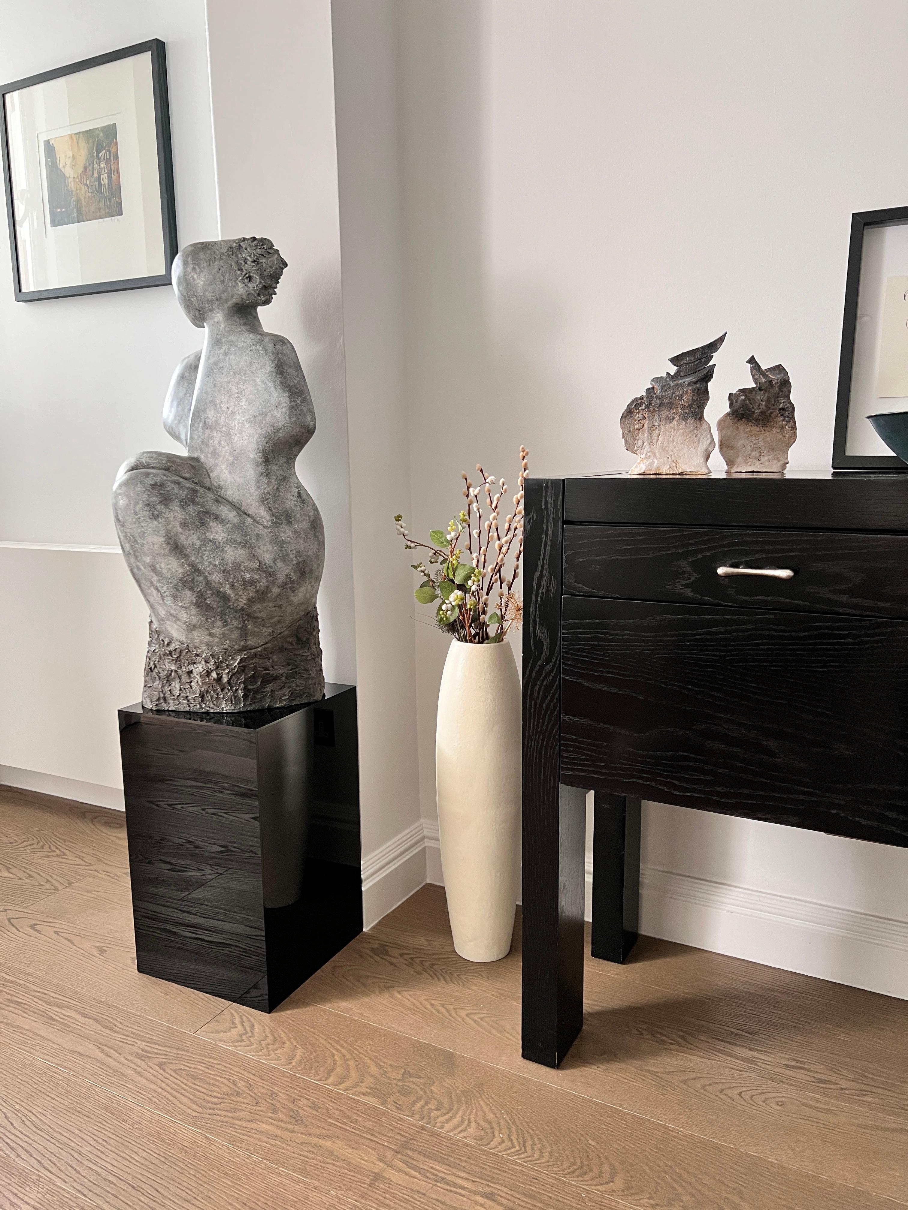 
Questa scultura astratta unica nel suo genere raffigura una donna seduta, realizzata a mano, modellata e fusa in resina di pietra. Il pezzo presenta una splendida patina nei toni del grigio muschiato, che imita l'aspetto  di pietra organica.
La