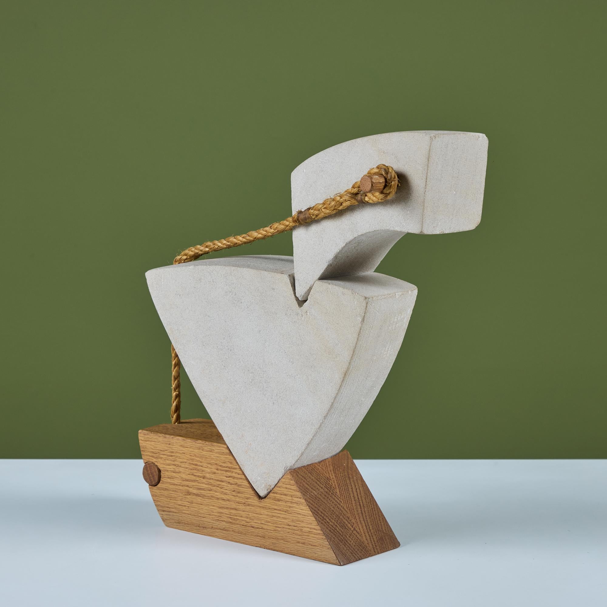 Scultura astratta in pietra nello stile di Noguchi. La scultura consiste in due pezzi di pietra incastrati l'uno nell'altro e poi bilanciati su una base di legno. L'opera utilizza anche una corda e dei pioli di legno per ancorare il pezzo e dargli