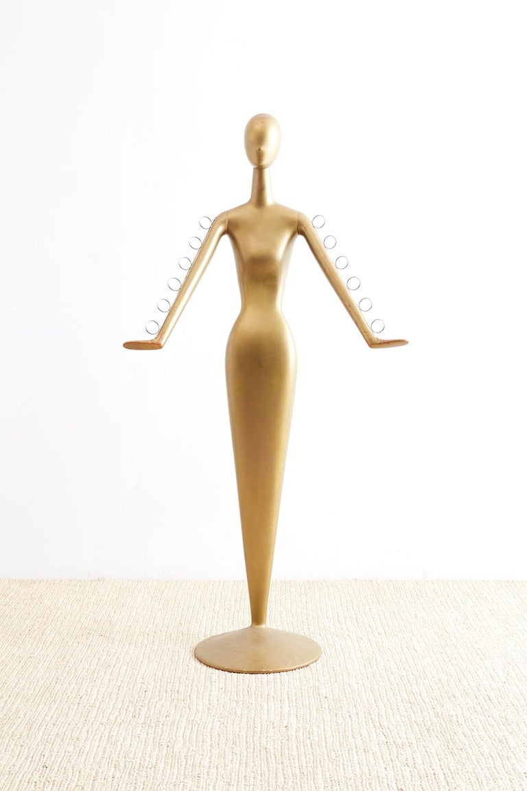 Atomic age abstract female display mannequin having a tulip form or mermaid style design. Constructed from fiberglass and finished in gilt over a coat of red lacquer. The svelte form has articulated arms that feature six chrome rings on each arm for