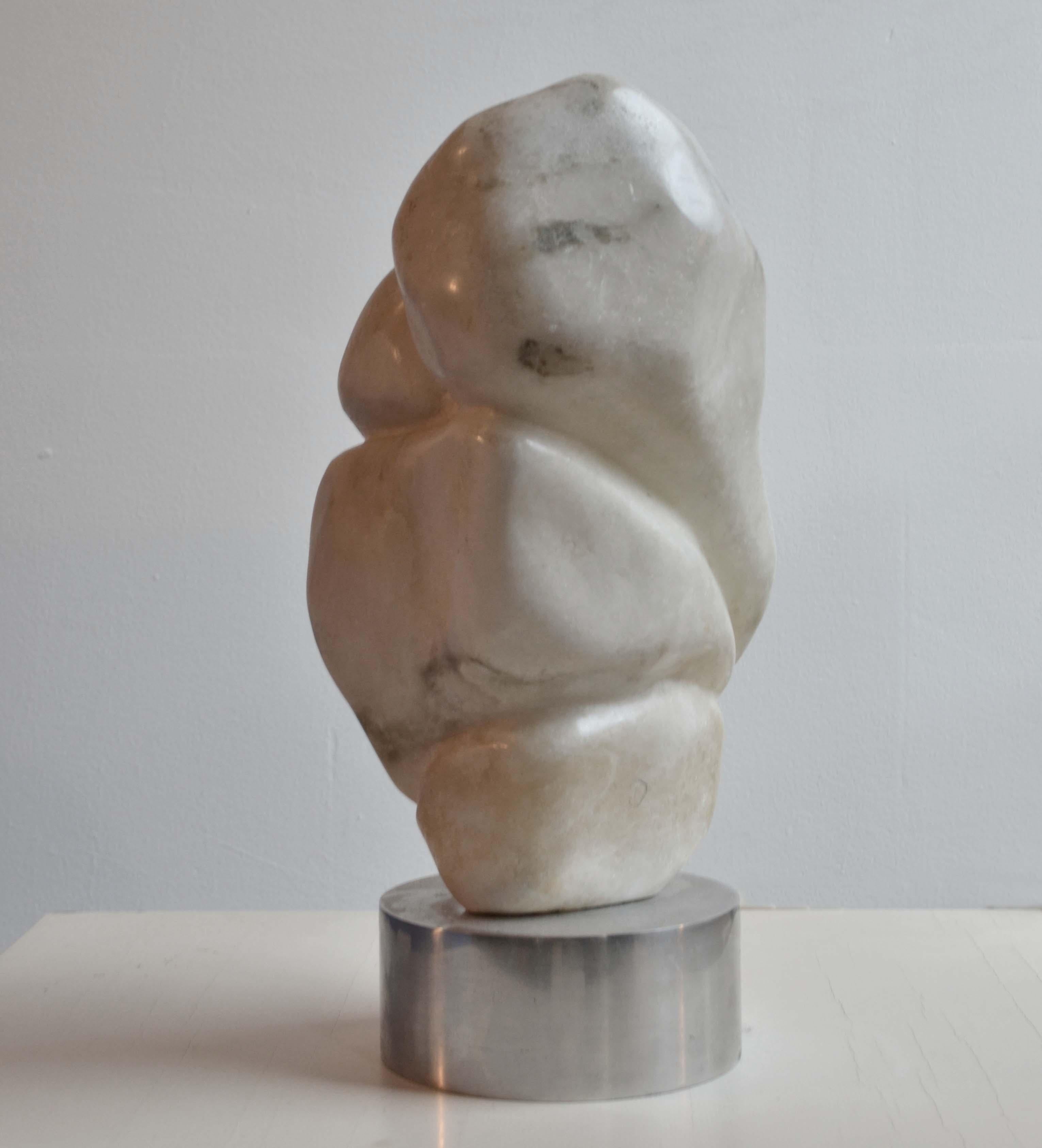 Hand carved curvaceous abstract sculpture in white marble with grey veins stands on a on a round aluminium plinth. From every angle it changes in shape and therefore it is perfect to be displayed in an open space. It is made by the late UK artist