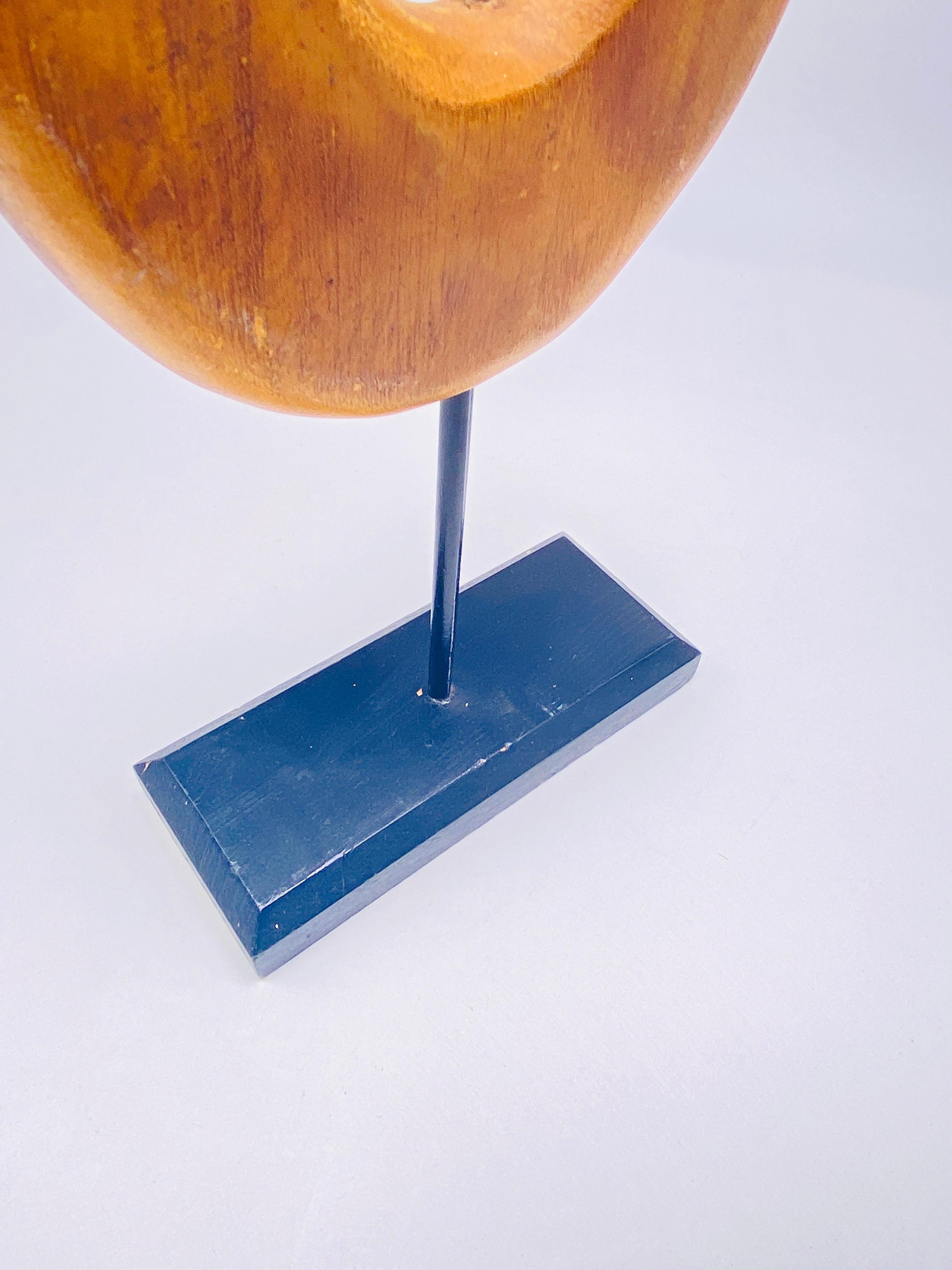 Si tratta di una scultura in legno curvo, di colore marrone chiaro. È stato realizzato negli anni '70 in Francia. Una barra di ferro dipinta di nero la fissa alla base, anch'essa in legno dipinto di nero. Si tratta di una scultura astratta.