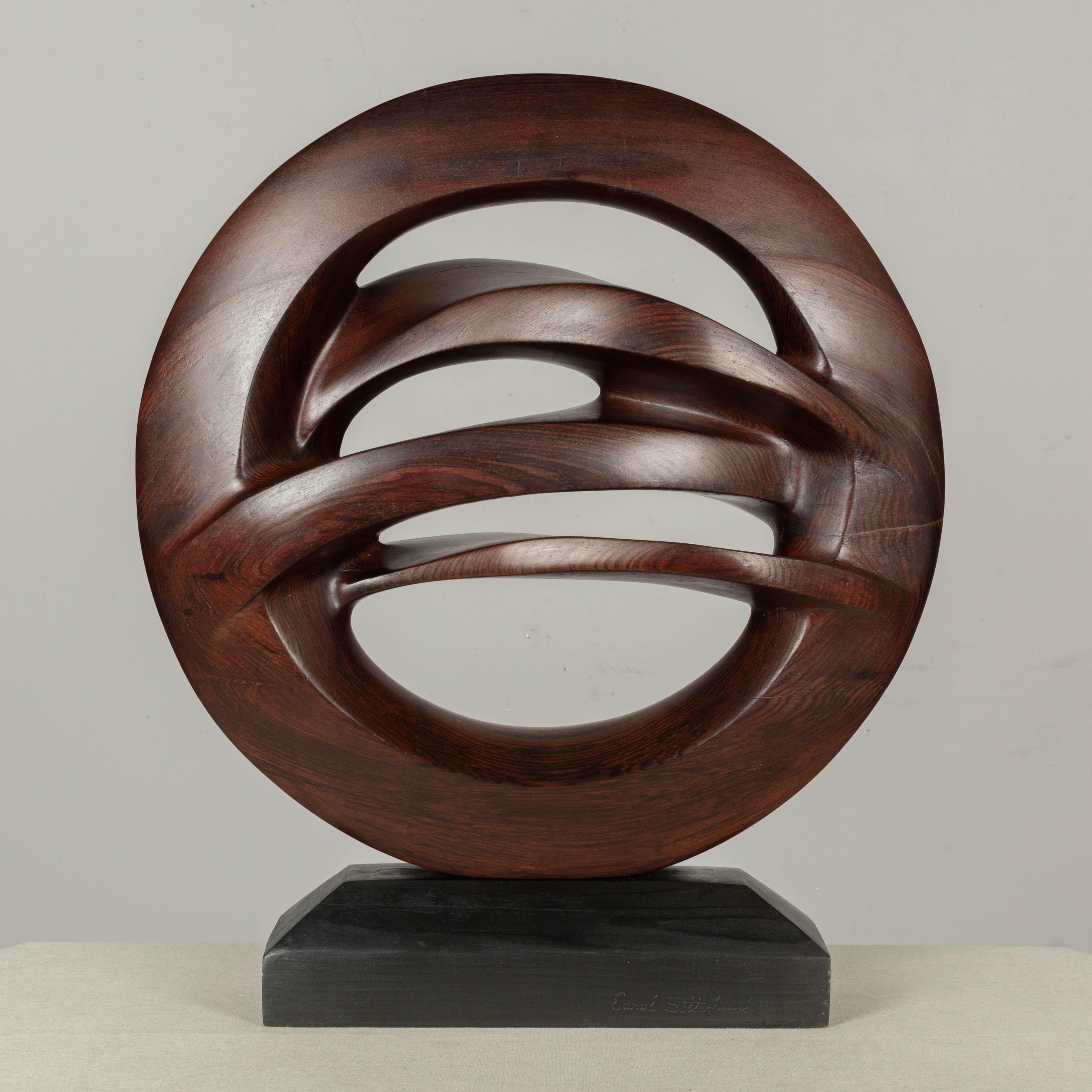 Abstract wood sculpture by California artist, Carol Setterlund (b. 1936). Smooth, organic form carved from old growth redwood, on a black rectangular plinth. Artist signature on base.
