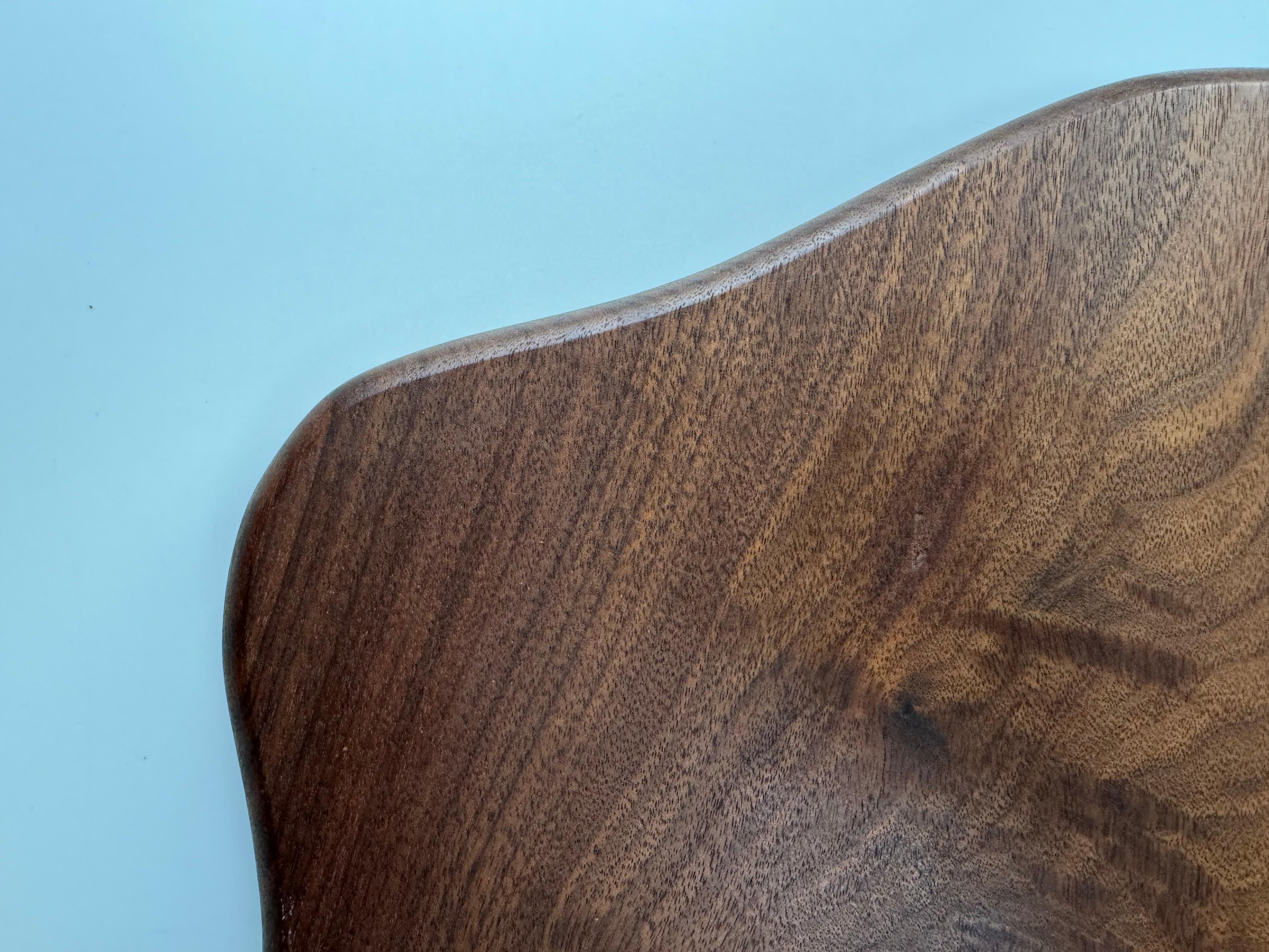 Dieses einzigartige und abstrakte Holzbrett aus amerikanischem Schwarznussholz hat eine Menge Charakter. 

Die Maserung, das Muster und die Farben dieses Holzes ergänzen die abstrakten Formen des Brettes. 

Es ist ein ideales Mittelstück für einen
