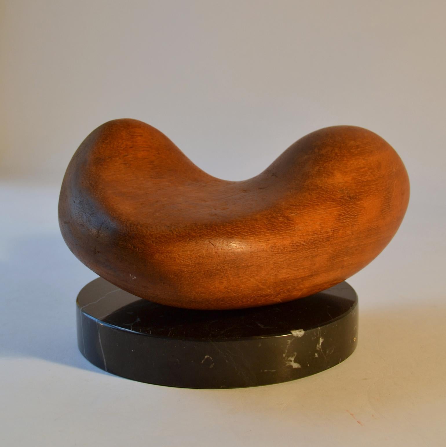 Abstract heart shape hand carved sculpture on a round black plinth. It curvaceous form is hand carved in hard wood and placed on a loose disk shape black marble base.

 