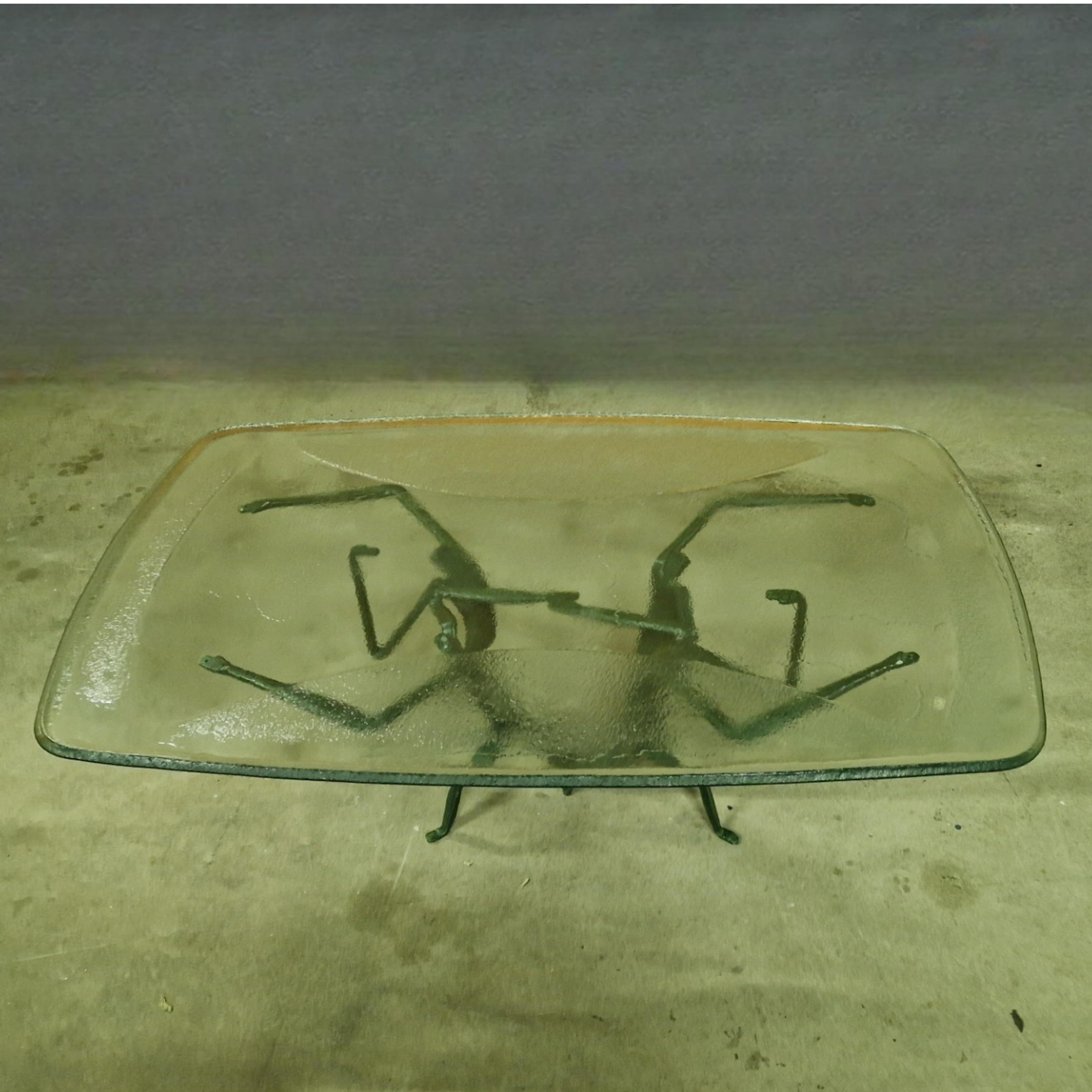 Unique handcrafted coffee table. The base is made from green painted wrought iron and it depicts 4 abstract figures with exceptional long limbs holding the top with their hands. The top is made from handmade textured glass with an upstanding edge.