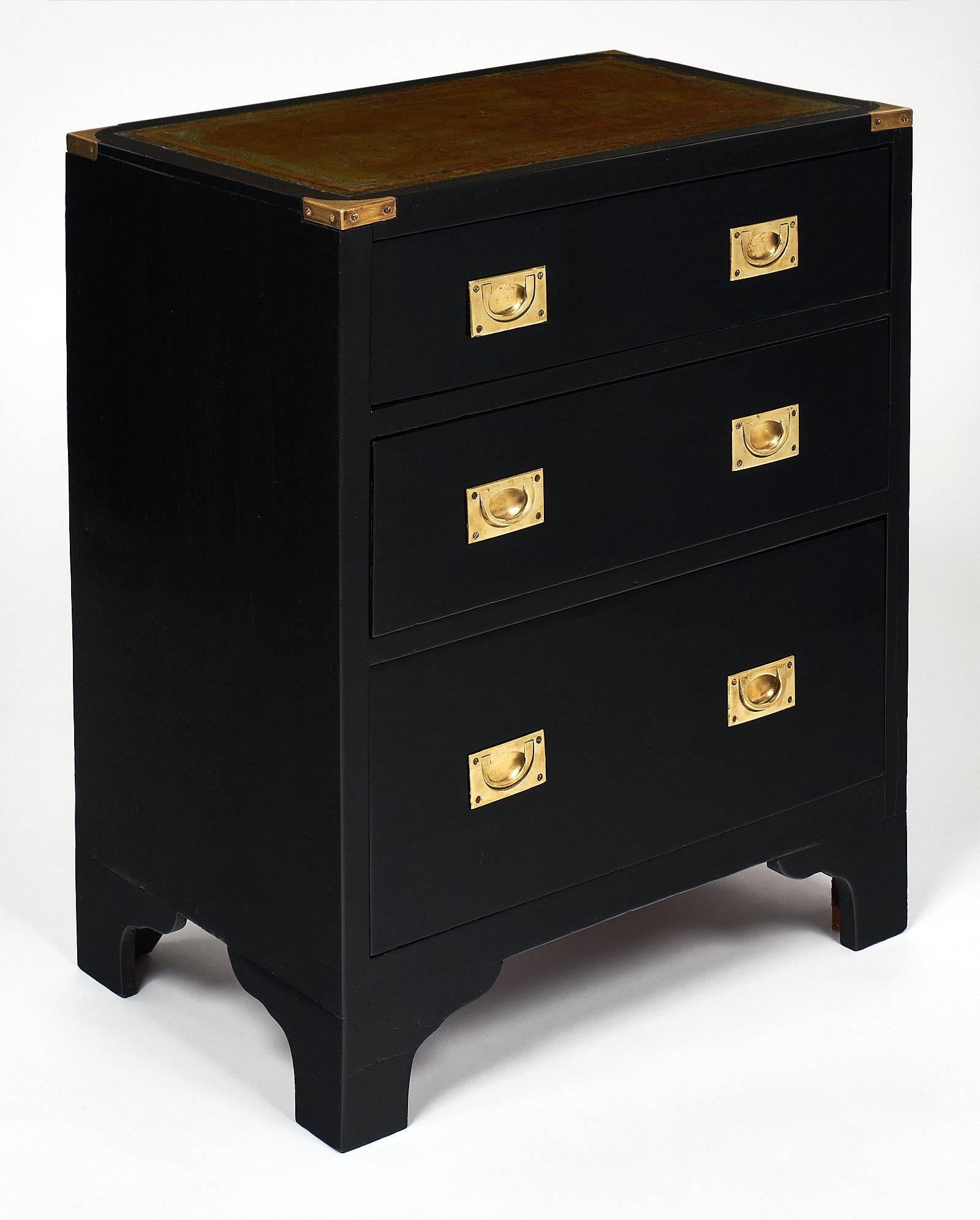 An antique English campaign chest of drawers of ebonized and French polished mahogany, oak as a secondary wood. This piece has three dovetailed drawers with two solid inserted gilt brass handles on each. The top is green Moroccan leather with gold