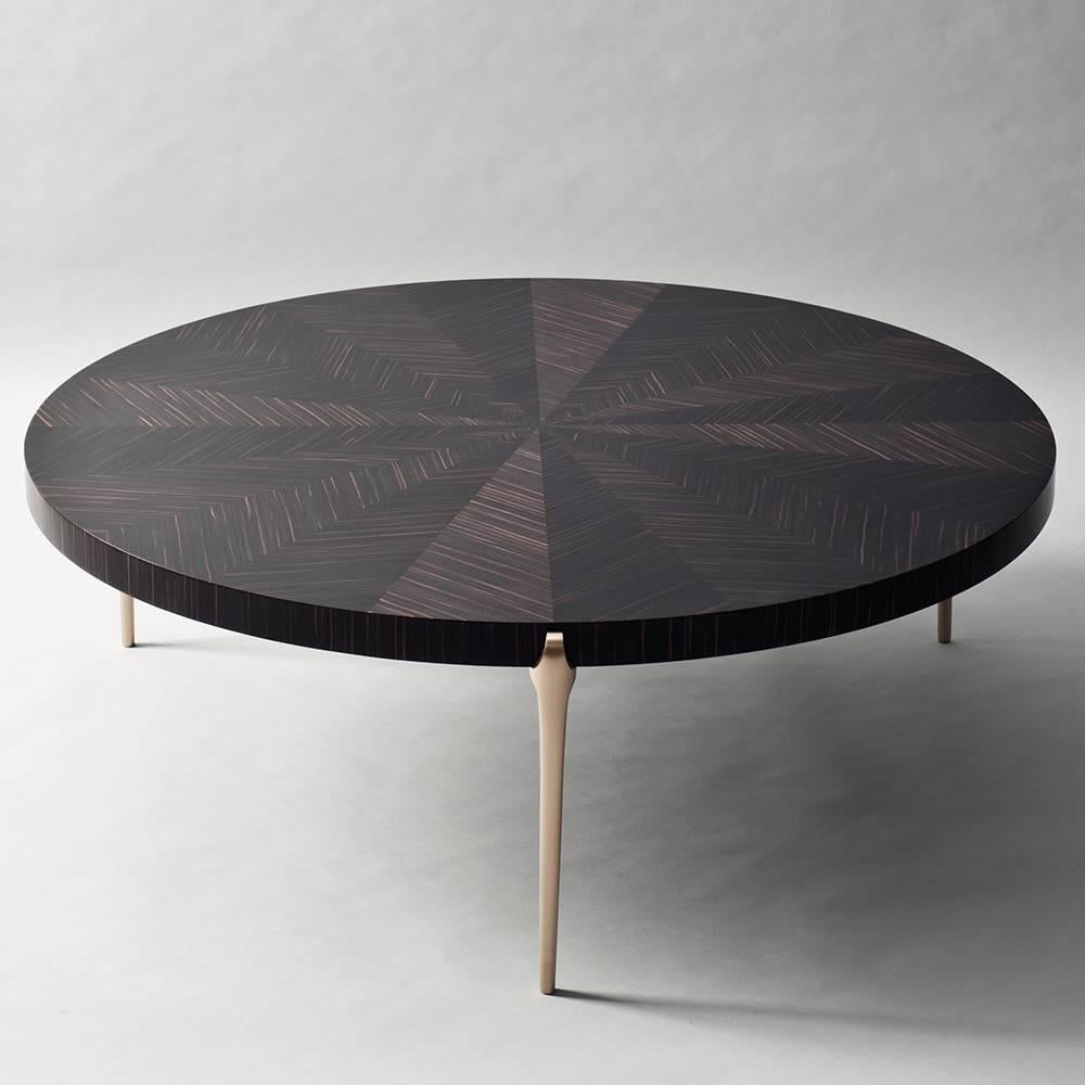Die Tischserie Acantha mit ihren sparsamen, runden Platten und schlanken, massiven Metallträgern ist eine Hommage an die Feinheit des Handwerks und den Reichtum seltener Materialien. Der Couchtisch zeichnet sich durch eine breite, durchgehende