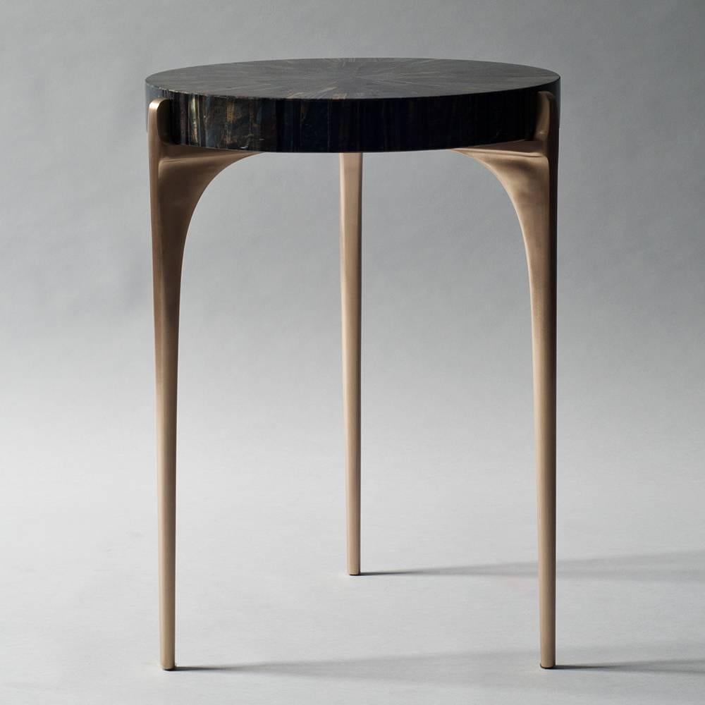 The Acantha side or end table by DeMuro Das features a circular top in blue tiger's eye, a semi-precious stone with striking blue, gold and brown coloration. This top is supported by three delicately tapered legs in hand-cast solid bronze.