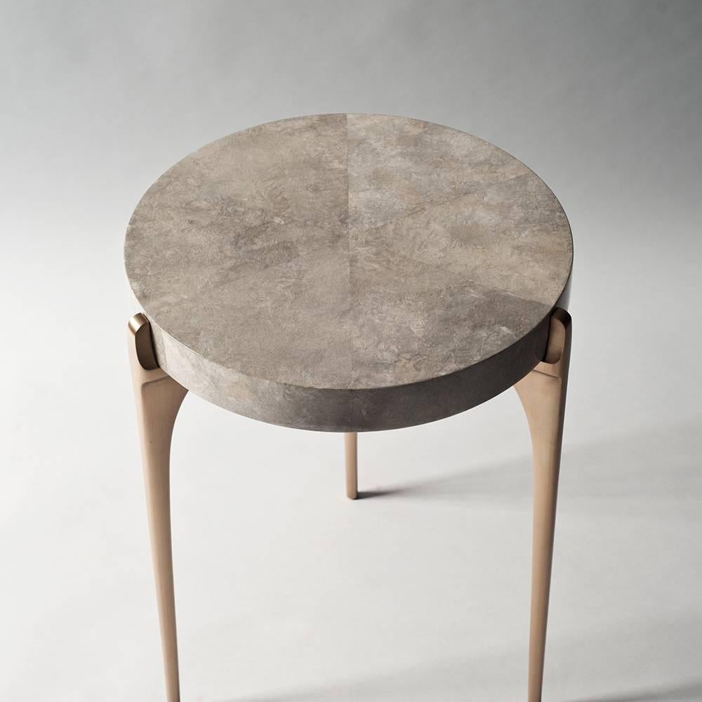 Die Tischserie Acantha mit ihren sparsamen, runden Platten und schlanken, massiven Metallträgern ist eine Hommage an die Feinheit des Handwerks und den Reichtum seltener Materialien. Der Beistelltisch hat eine medaillonartige Oberfläche, die auf