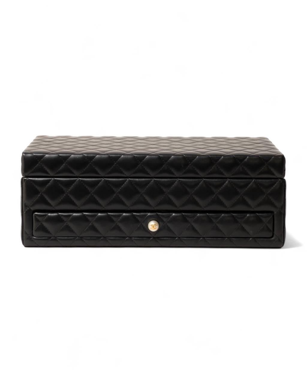 Portagioie firmato Chanel, modello Vanity Case Pearl, realizzato in pelle d’agnello trapuntata nella colorazione nera con hardware dorati. Internamente rivestito in tessuto scamosciato e minuteria metallica dorata, specchio centrale sulla parte