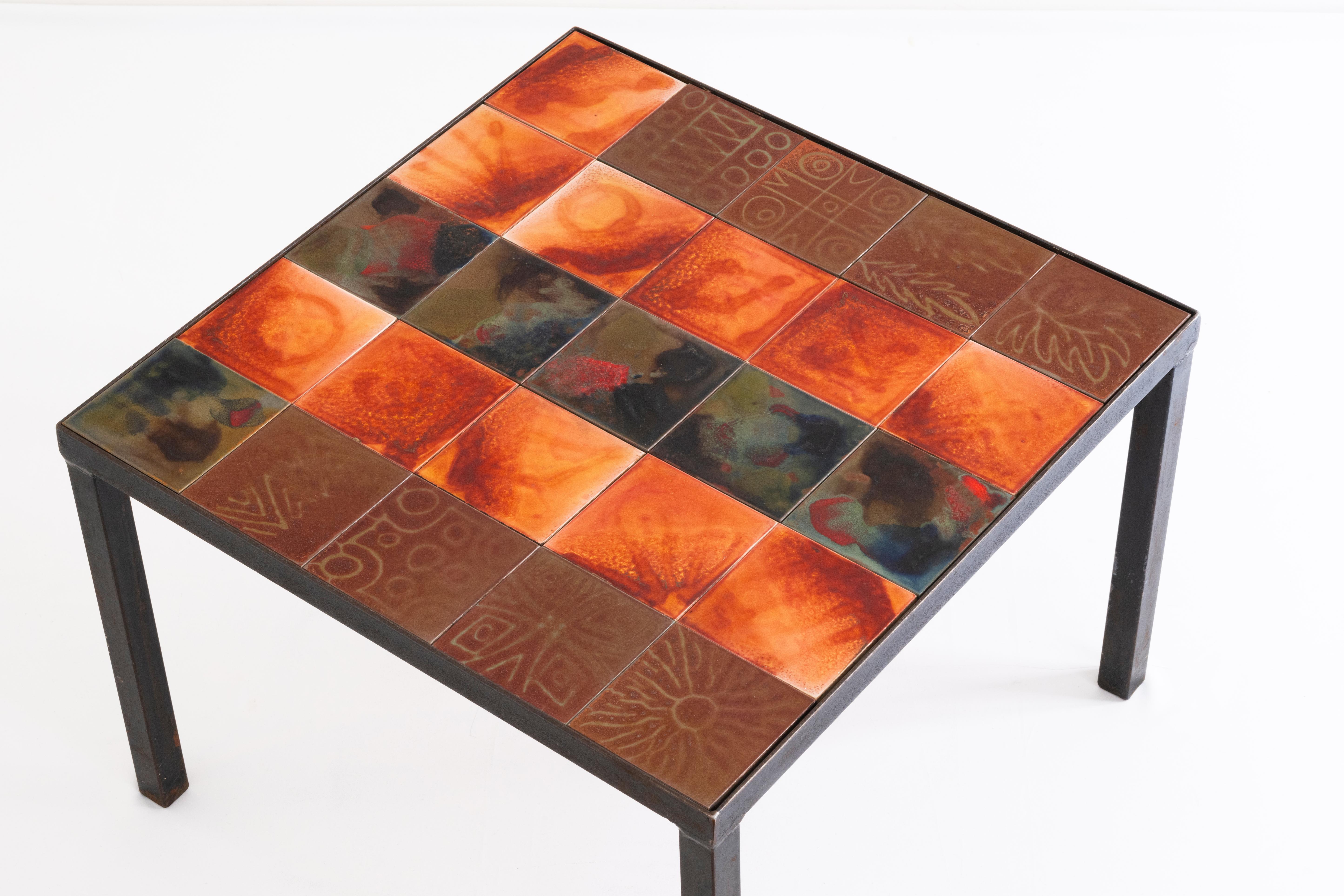 Cette étonnante et unique table basse en fer, attribuée à Accolay, est un mélange unique d'art et d'utilité. Son plateau carré en bois est composé de vingt carreaux de céramique amovibles, chacun orné de motifs stylisés ou végétaux, apportant une