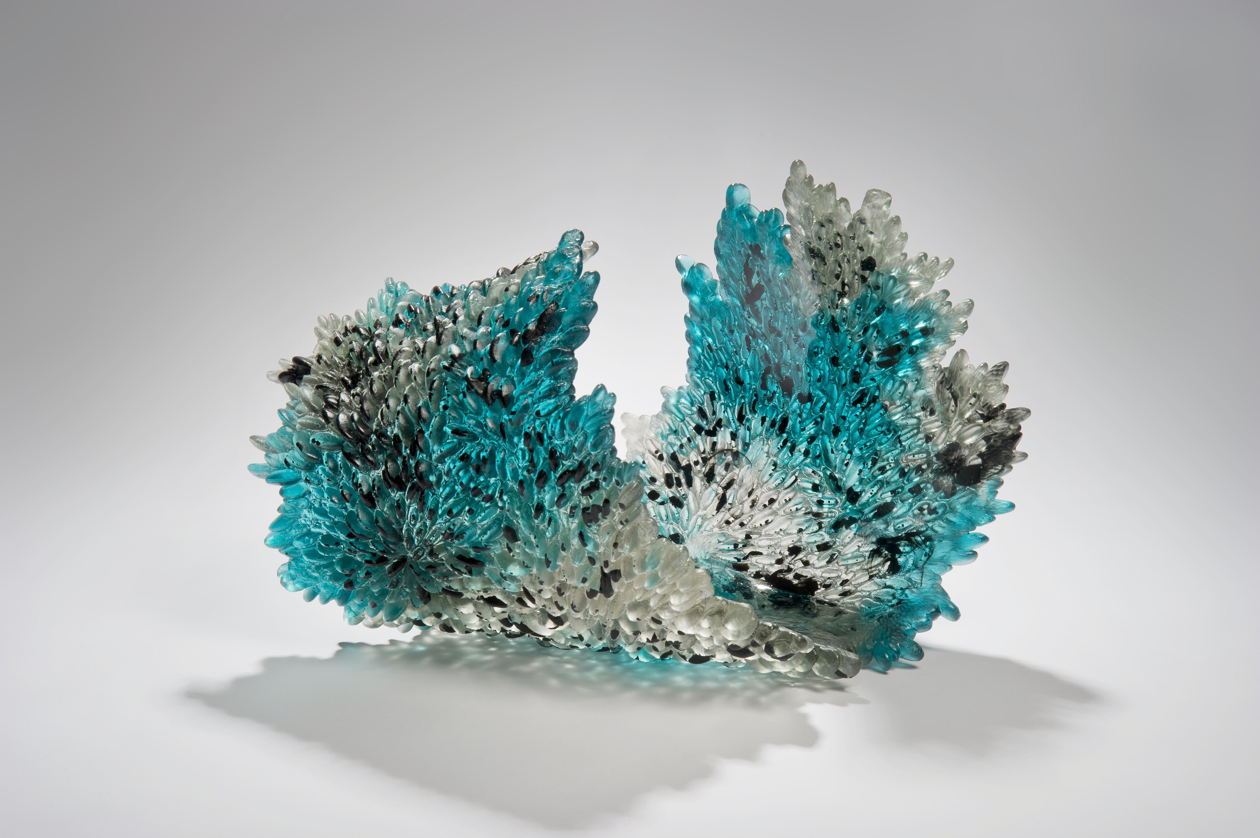 Acculturation is a unique textured glass sculpture in clear, teal and black by the British artist Nina Casson McGarva. 

Casson McGarva firstly casts her glass in a flat mould where she introduces all of the beautifully detailed, scaled surface