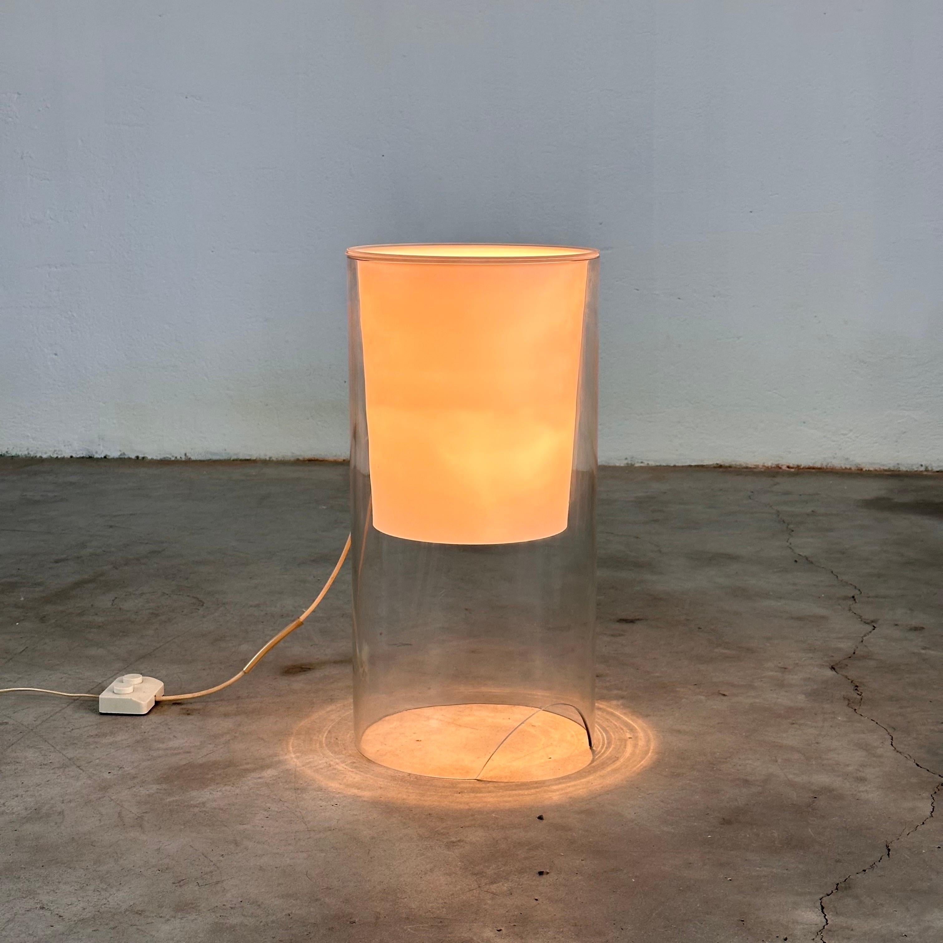 
Cette lampe de table présente un corps extérieur cylindrique en verre clair. Un diffuseur/réflecteur en verre opale blanc se trouve à l'intérieur du cylindre sur la partie supérieure du corps. La lampe est fabriquée en verre soufflé à la main, sans