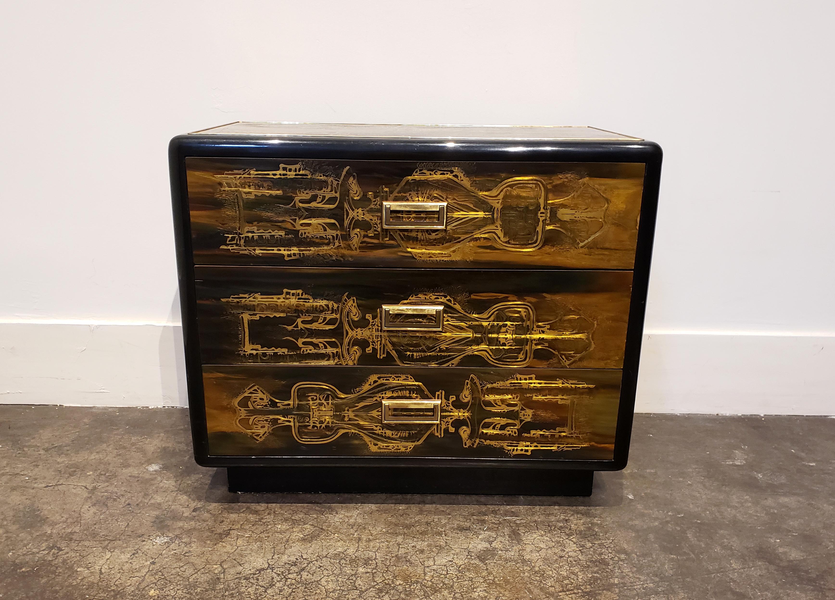 Rare model Bernhard Rohne chest for Mastercraft. Acid-etched brass with multi-colored epoxied surface which positively glows in light, set into and accentuated by glossy black lacquer. Has three drawers with brass pull handles.
 