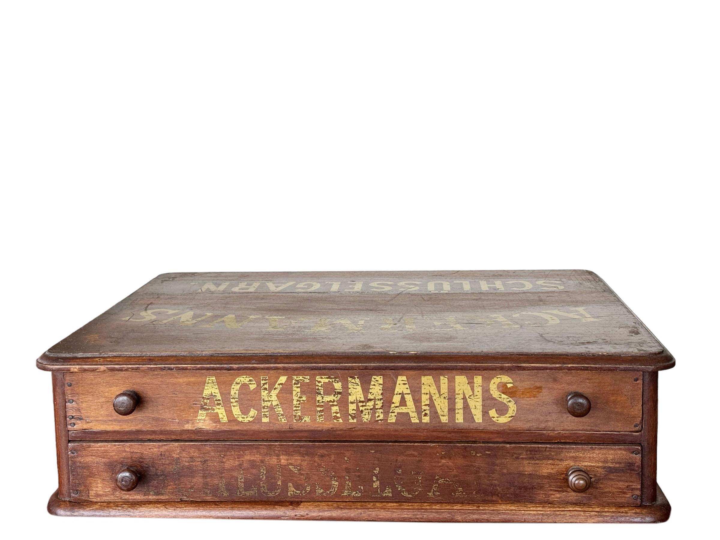 An early 19th century German advertising cabinet. Cabinet with two drawers with gold writing on the top and drawers that reads Ackermanns Schlusselgarn. It appears it would have been on the counter so the top would face the customer for them to read