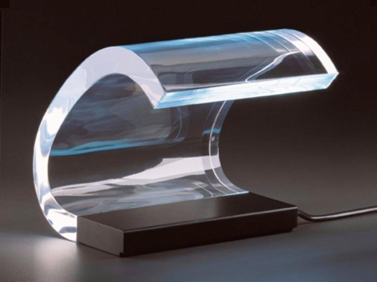 The Oluce Acrilica 281 is a table lamp, with a transparent, wavy diffuser fixed laterally on a steel base. It was created in 1962 and designed by Gianni as well as Joe Colombo. The energy-saving lamp is hidden in the base of the lamp. This lamp was