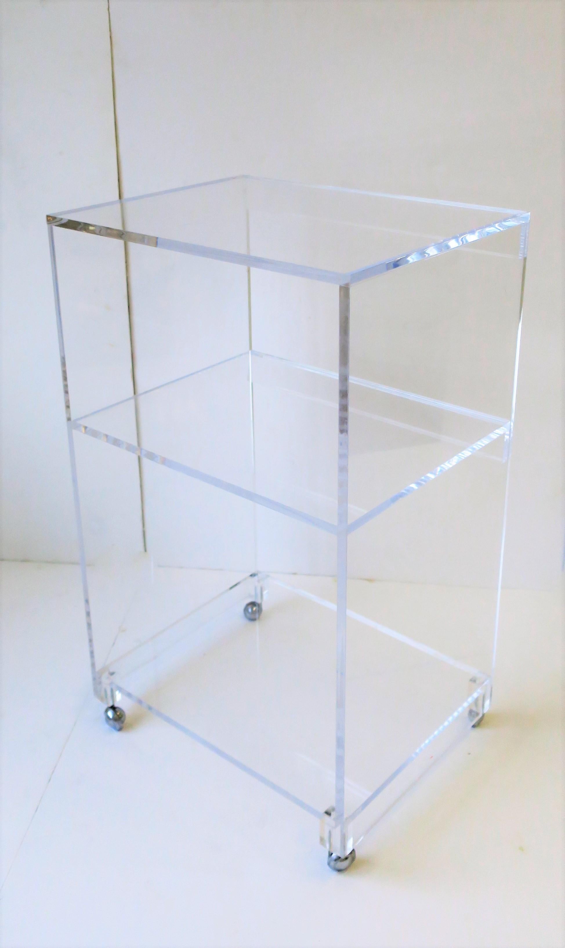 A substantial Lucite/acrylic bar cart, storage shelf, bookcase or cabinet on caster wheels. Piece has three shelf areas; top, middle and lower shelf. 

Piece measures: 30