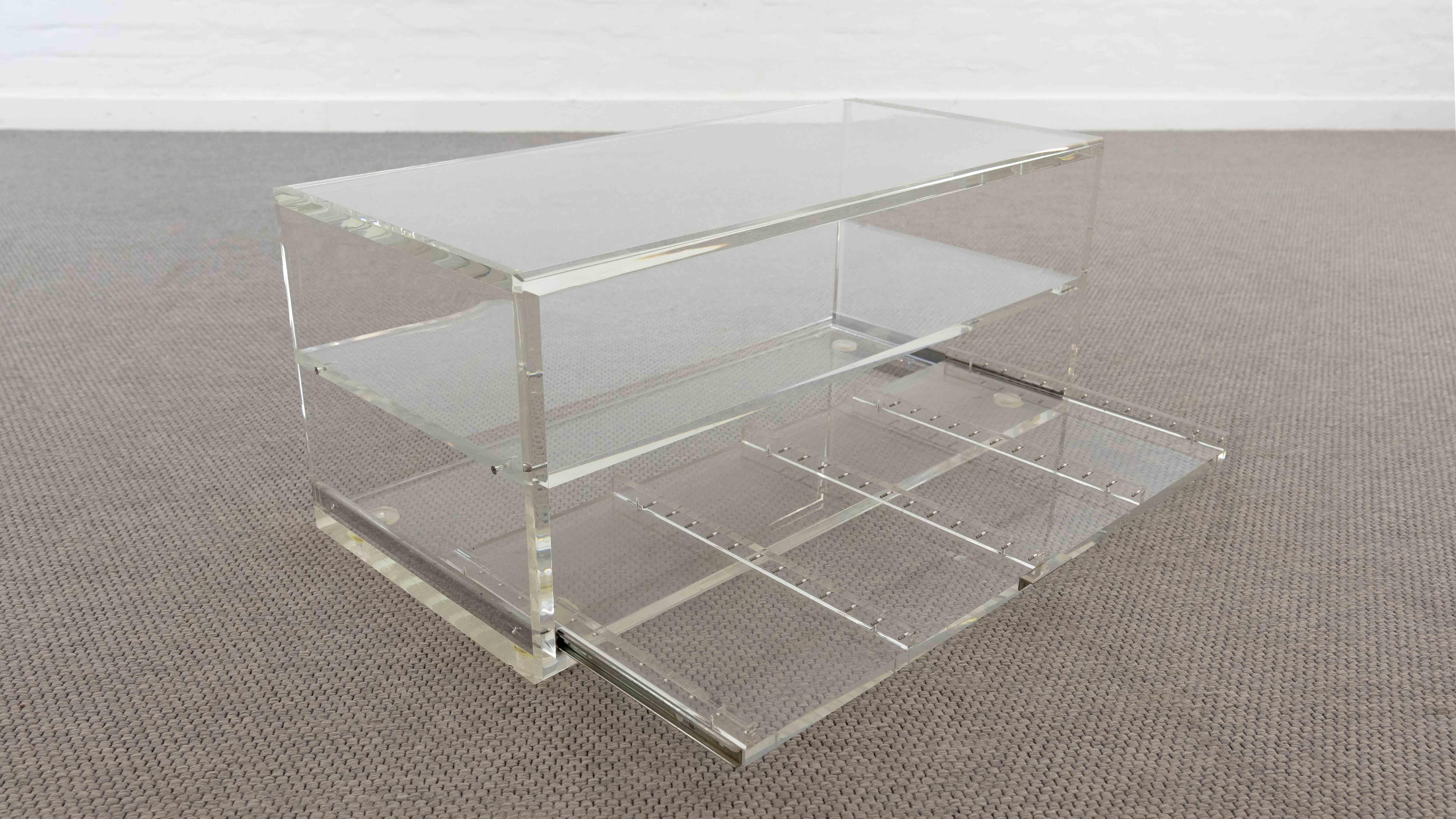 Transparent coffee or sofa table made of Acrylic / Plexiglass. 80s. Designer and Manufacturer unknown. Table with lower drawer to hold your Video Cassette Collection. Weight: 35KG. The Baltenweiler Table Lamp is not part of this offer.