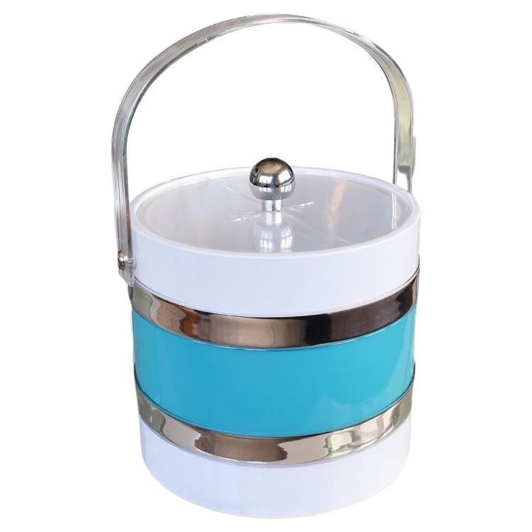 A fun round Mid-Century Modern ice bucket with a lid and acrylic handle. This bright colorful vintage ice bucket will be great on a bar at your next cocktail party. It is created from plastic and has a bright white exterior. Around the body, is a