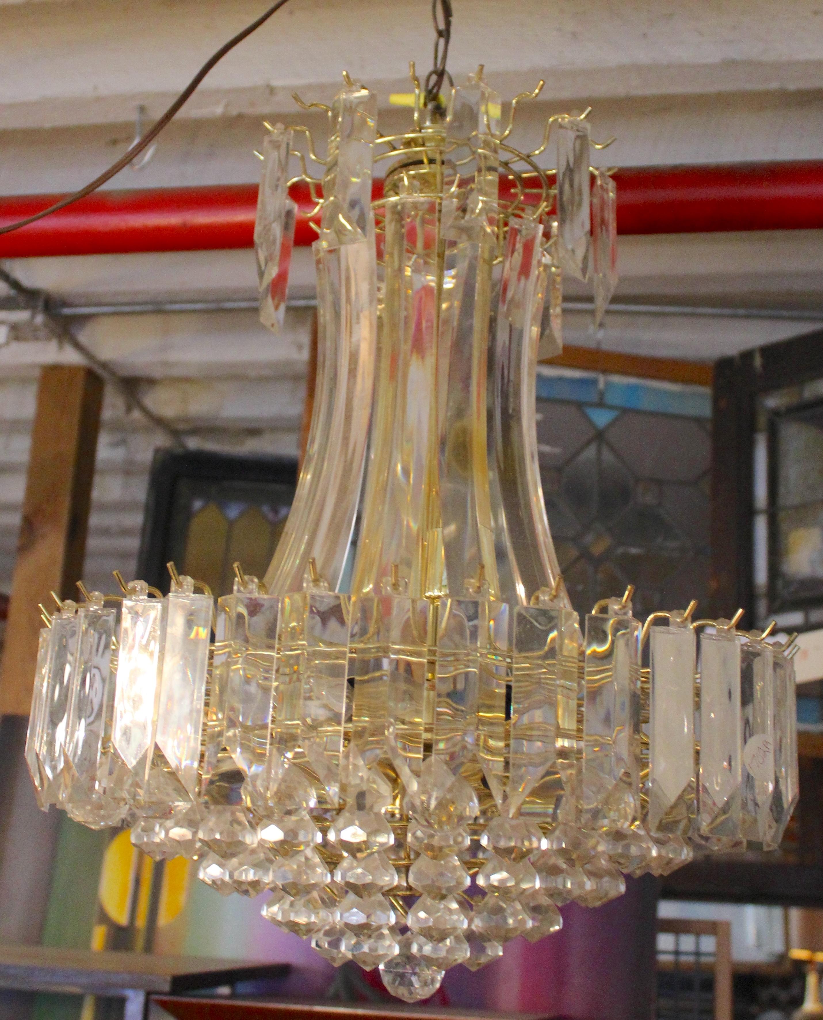 Questo grande lampadario a sospensione presenta un motivo a cascata di prismi in acrilico trasparente incastonati su una struttura in ottone. Otto prese in un diametro di 21