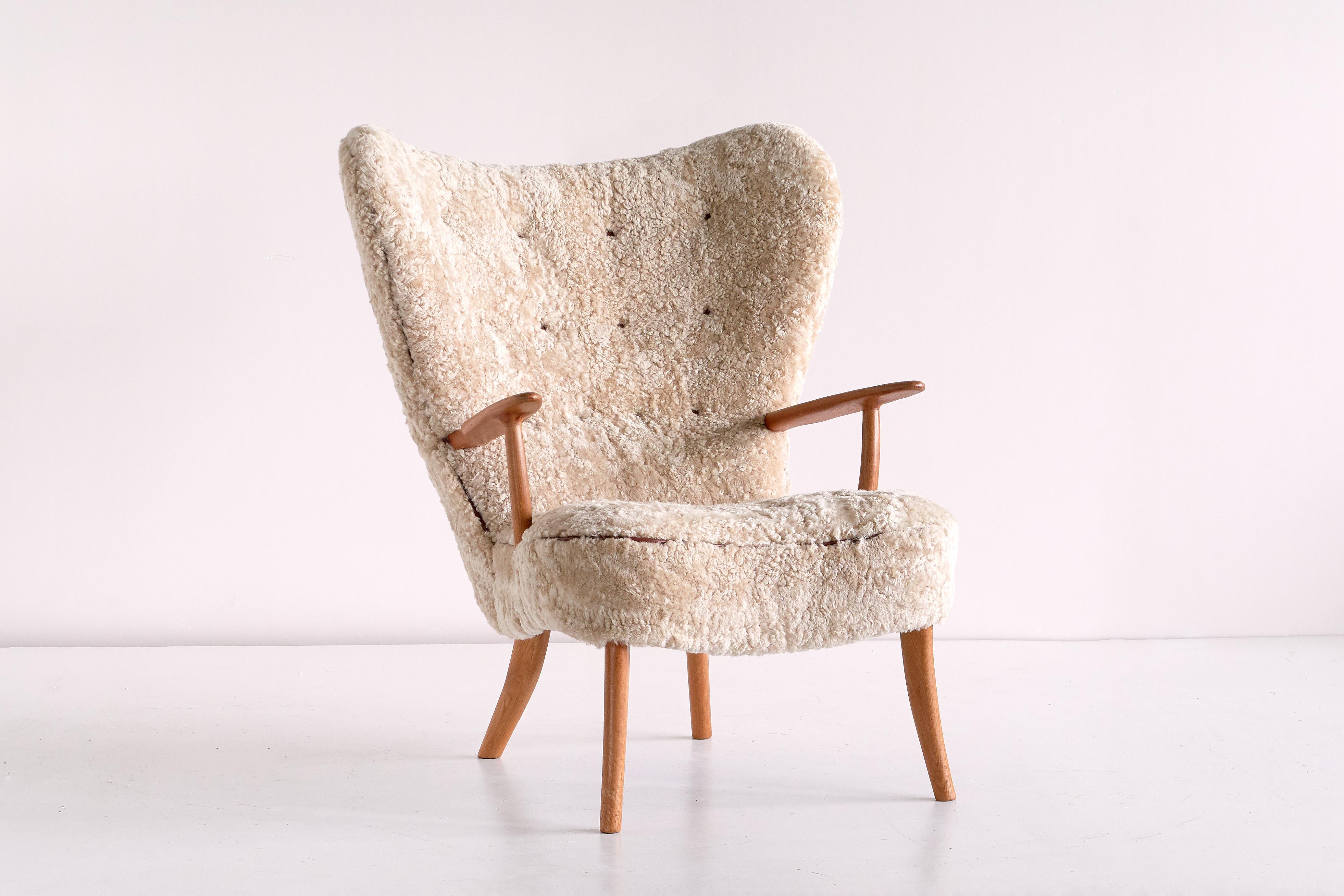 The rare 'Pragh' wingback chair was designed by Acton Schubell and Ib Madsen in the early 1950s. The generously sized chair has been fully reconditioned and newly upholstered in a sand colored, naturally curly and soft sheepskin. The high back and
