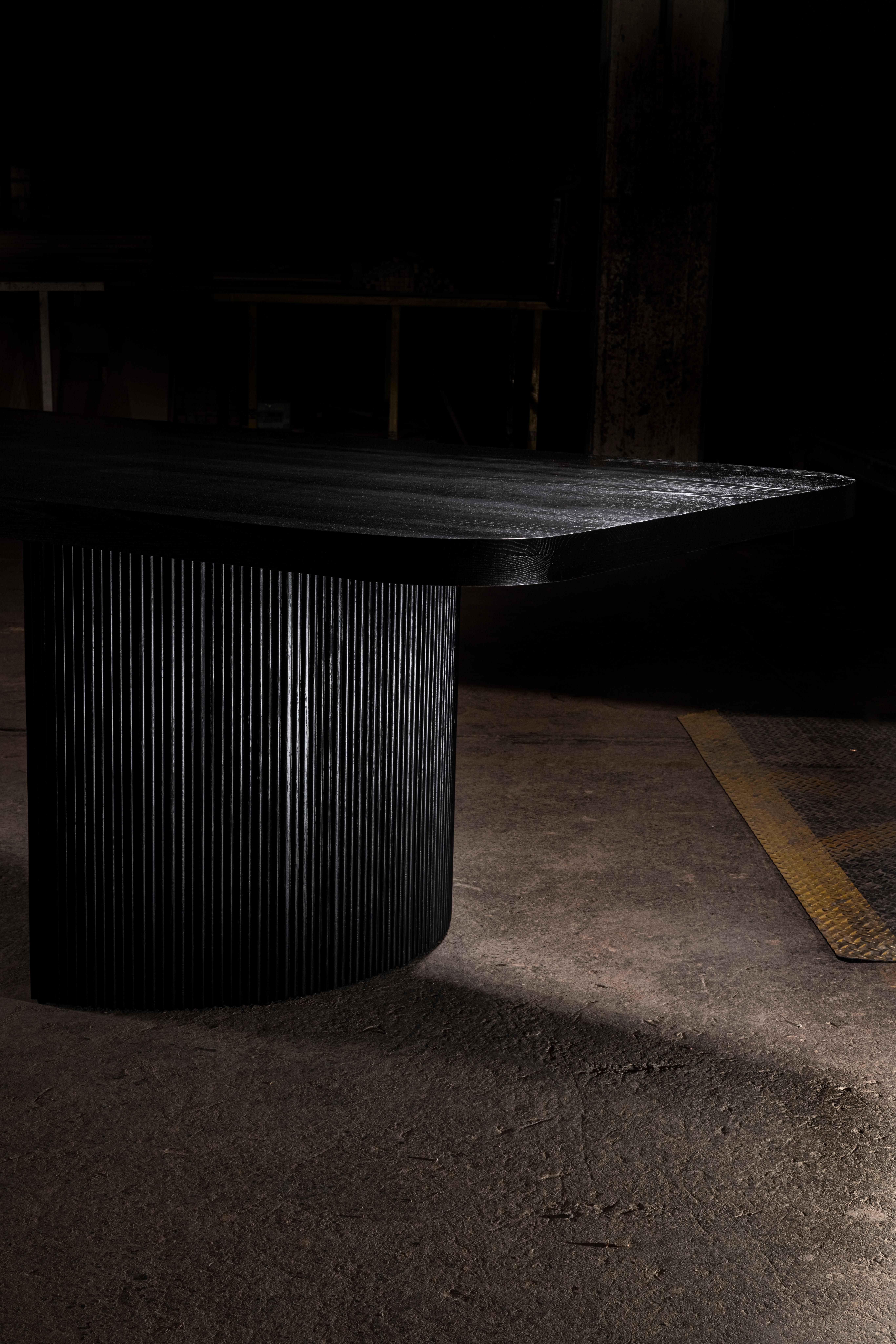 Black oak dining table with rounded corners, pedestals are half circle with fluted wood detail.