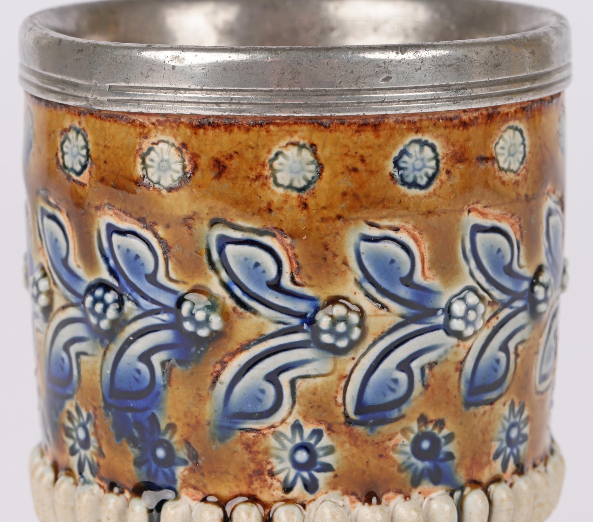 A stunning Aesthetic Movement Doulton Lambeth floral design pewter mounted beaker shaped vase by Ada Tosen and dated 1883. The vase is decorated with two bands of stylized blue foliage set between small flower heads and separated by a band of raised