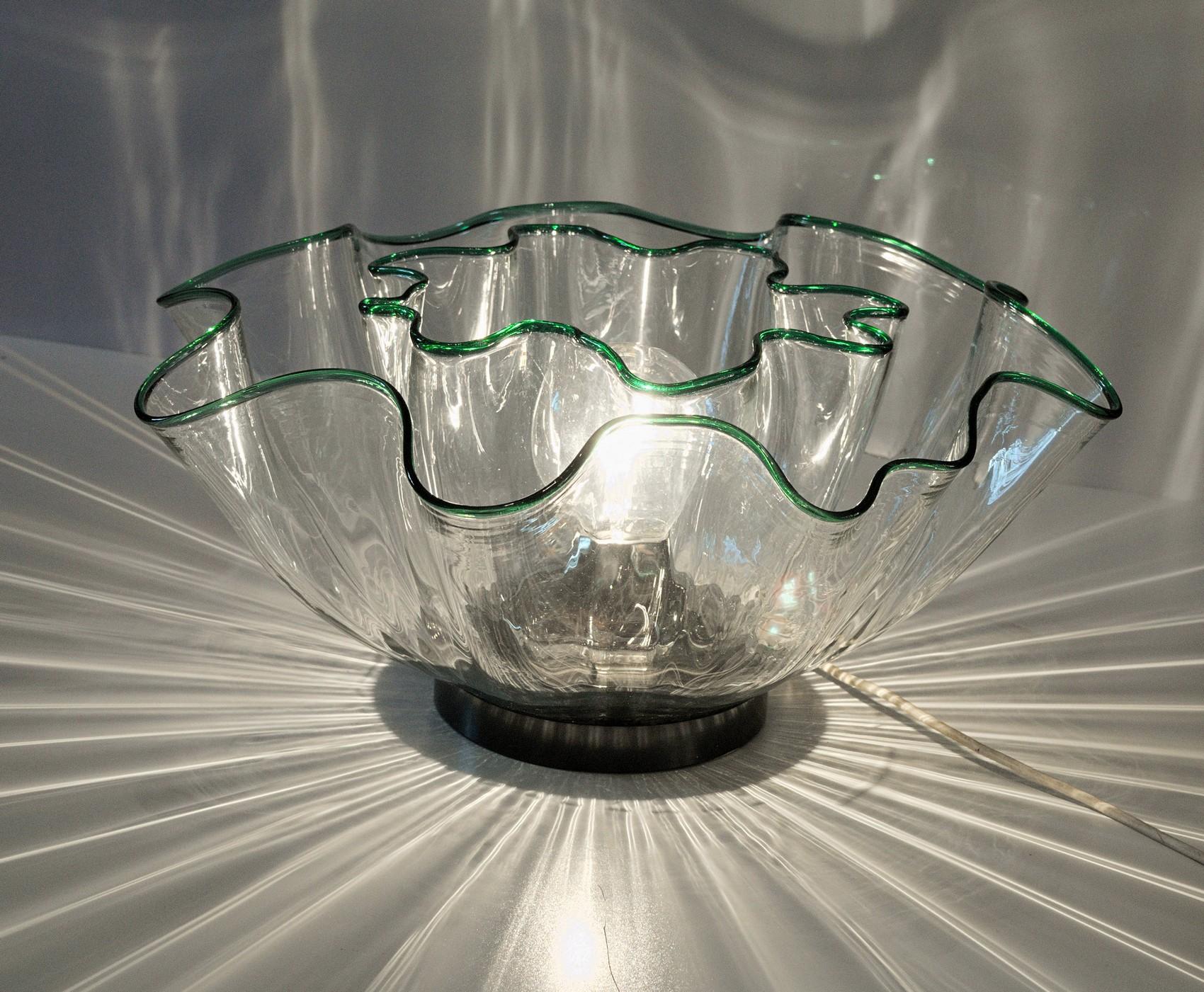 Beautiful lamp designed by Adalberto Lago and Stefania Giannotti for Vistosi. Made by two fazzoletto shape nested one into the other.
Green rim gets highlighted by the light. The two waved shapesare creating a sunburst effect with light.
Often sold