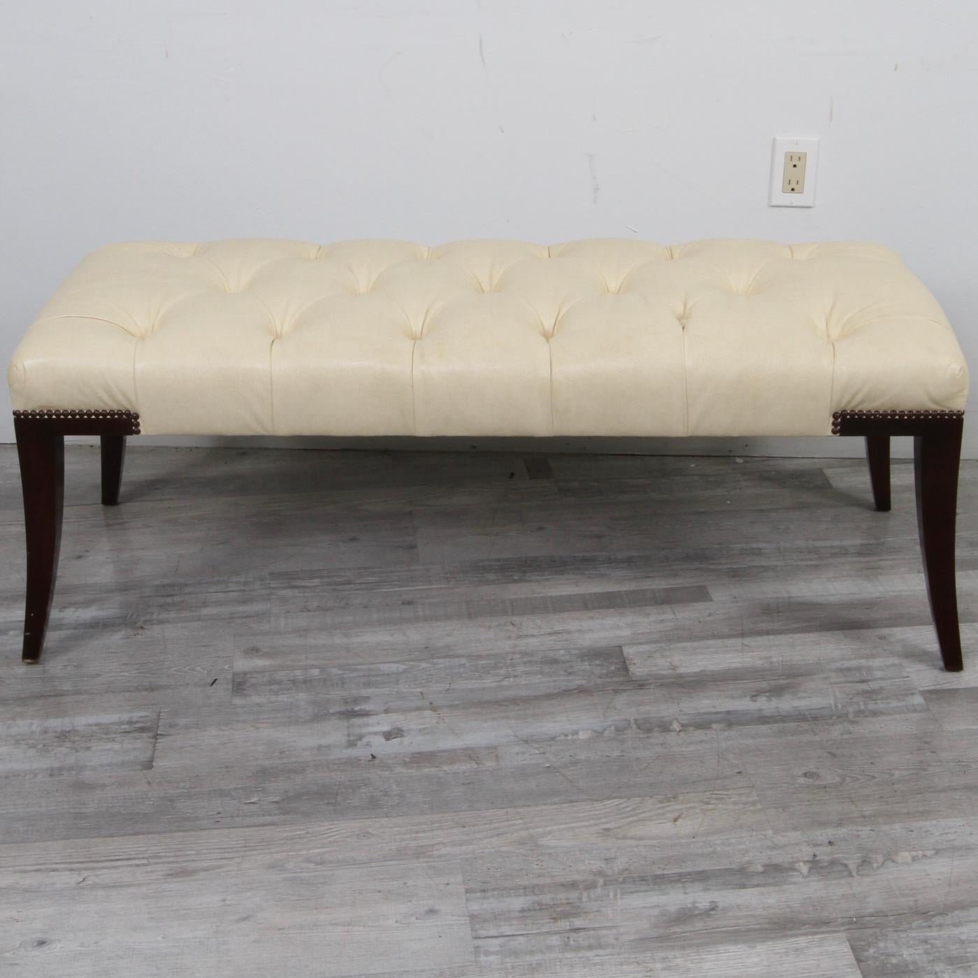A tufted ivory leather bench by Baker Furnture. Curved + tapered legs are in finished with a nailhead detail and espresso stain. Tufted upholstery is fabricated in a soft and warm neutral leather. Beautiful bench designed by Thomas Pheasant and