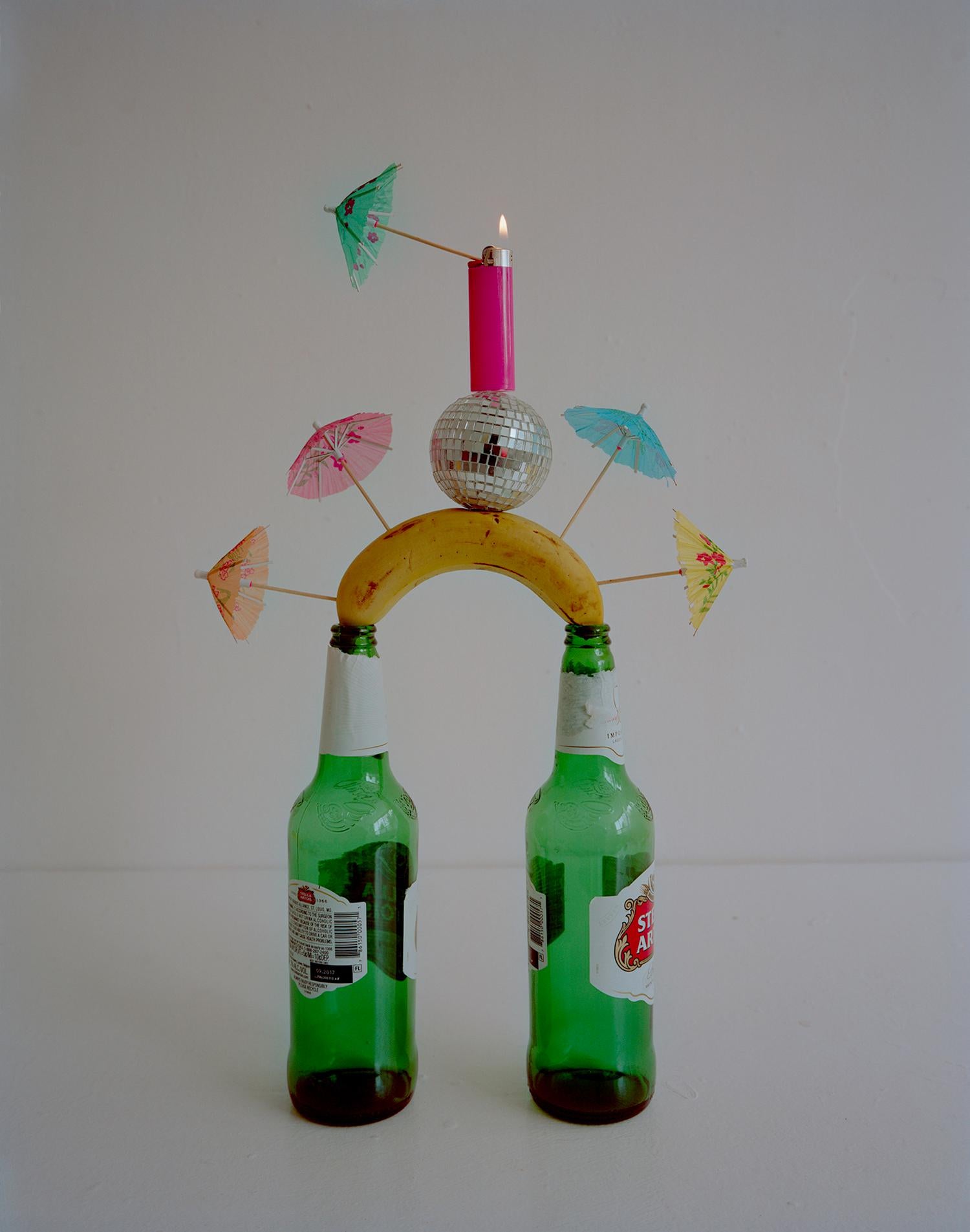 Adam Ekberg Still-Life Photograph - Beer Bottles, Banana, Cocktail Umbrellas, Disco Ball and Bic Lighter