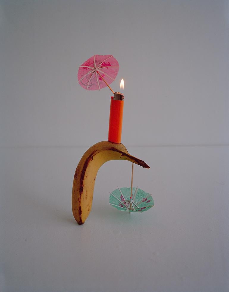 Adam Ekberg Color Photograph - Bic Lighter, Banana and Cocktail Umbrellas