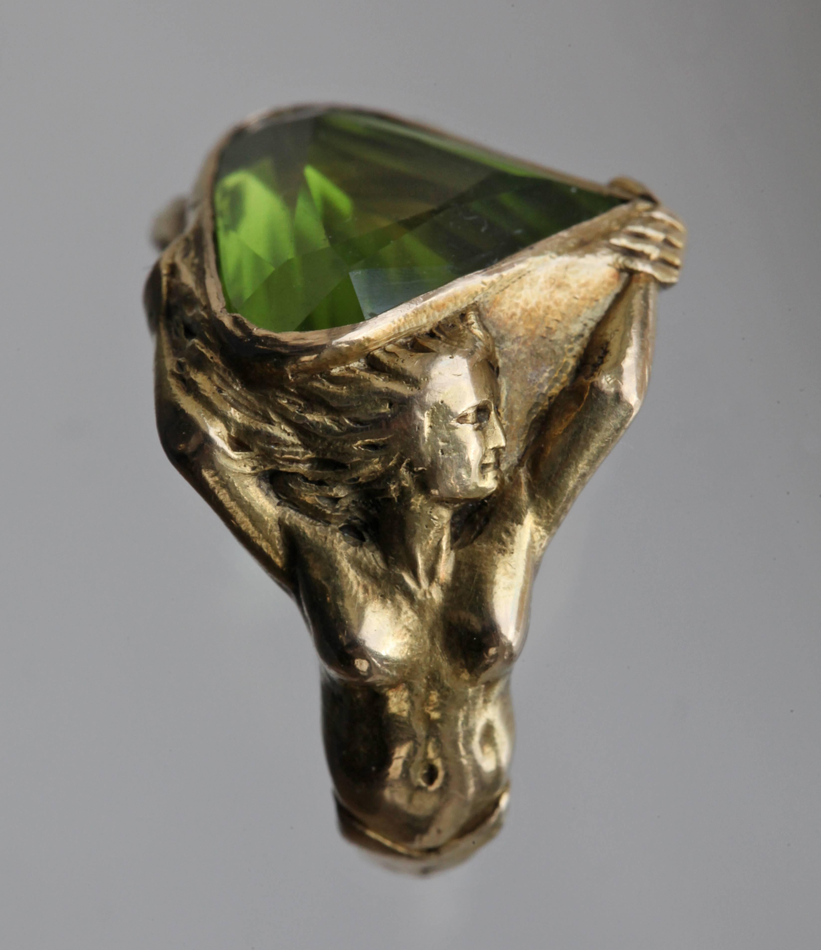 A wonderfully powerful erotic ring. The sculptural form portraying Adam & Eve clasping hands symbolizing original love. The ring shank resembles the belly of the serpent. The peridot has the colour of the forbidden fruit & the shape implies sexual