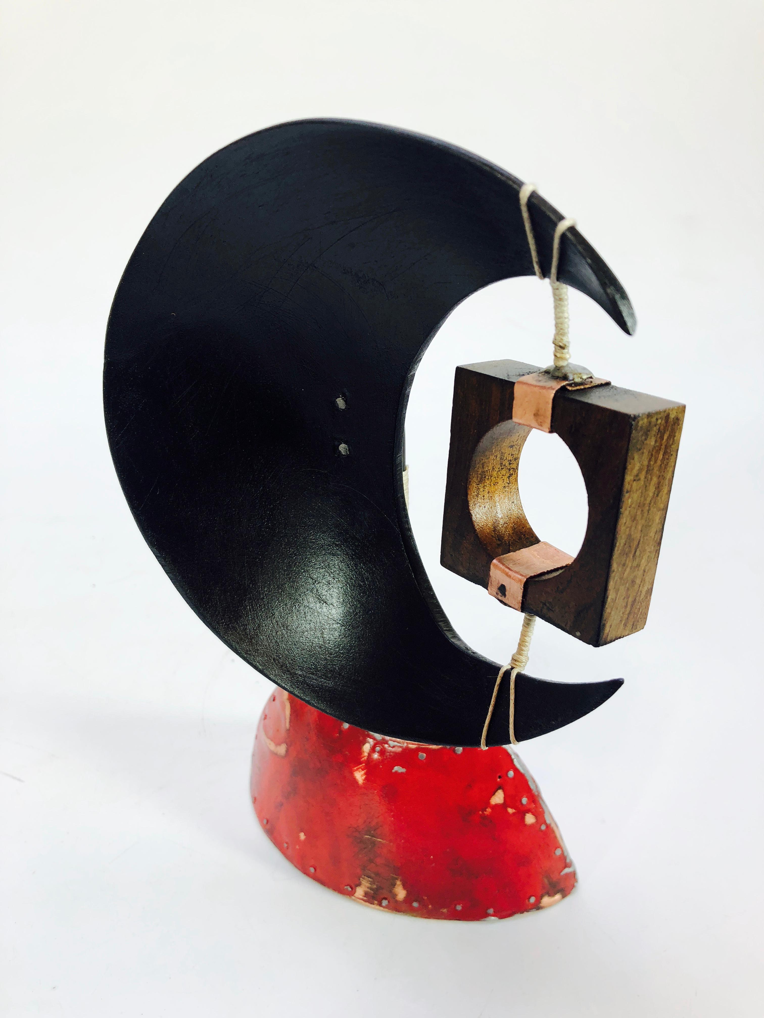 Adam Henderson's Cheers to Hell abstract sculpture of a partial moon shaped concave disc supported by an enameled copper base. The moon shape supports a suspended square with drilled circle.