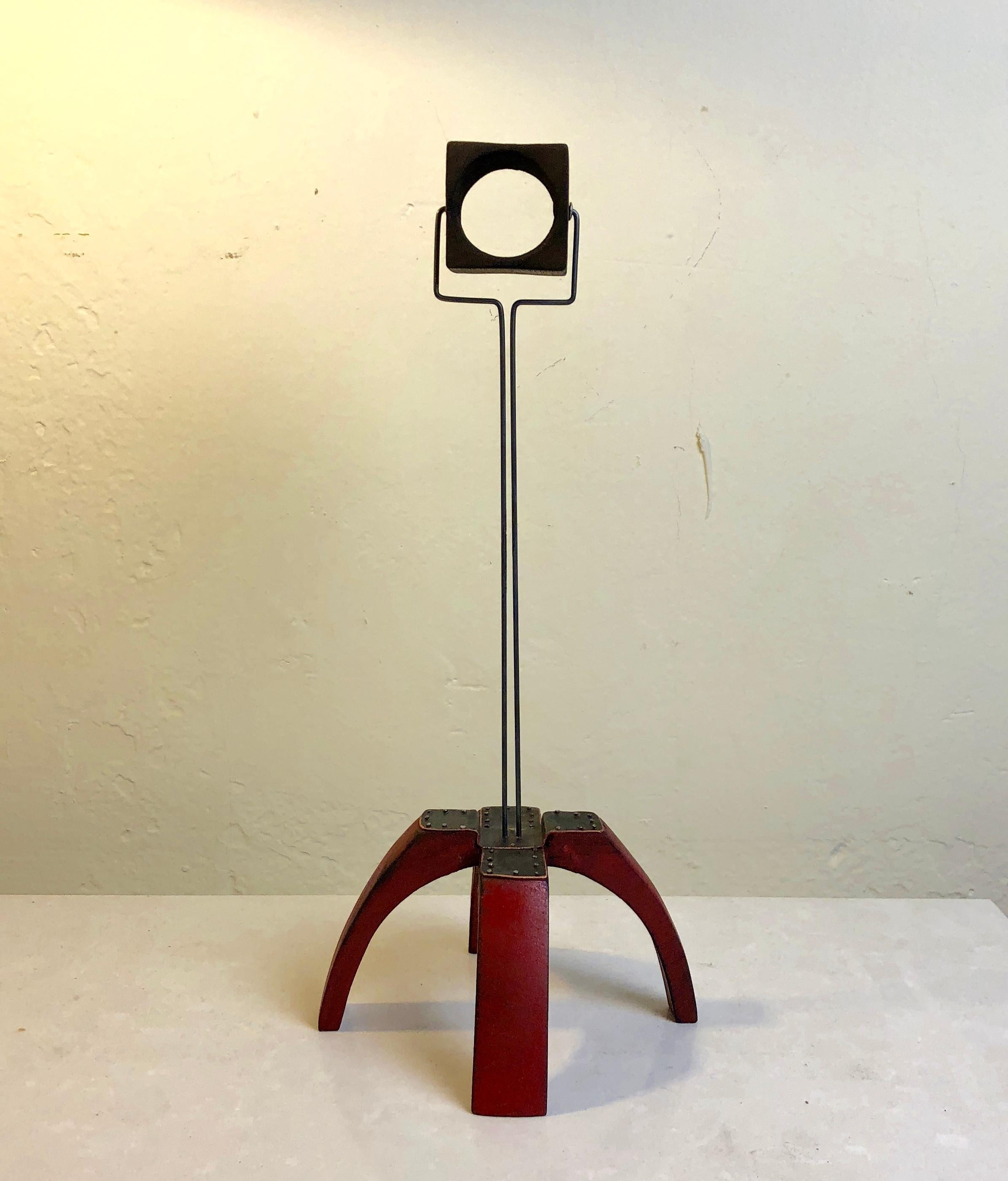Adam Henderson's high tower abstract sculpture of wood, sheet metal and wire. A movable cube supported by wire above a four legged base of stained red wood.