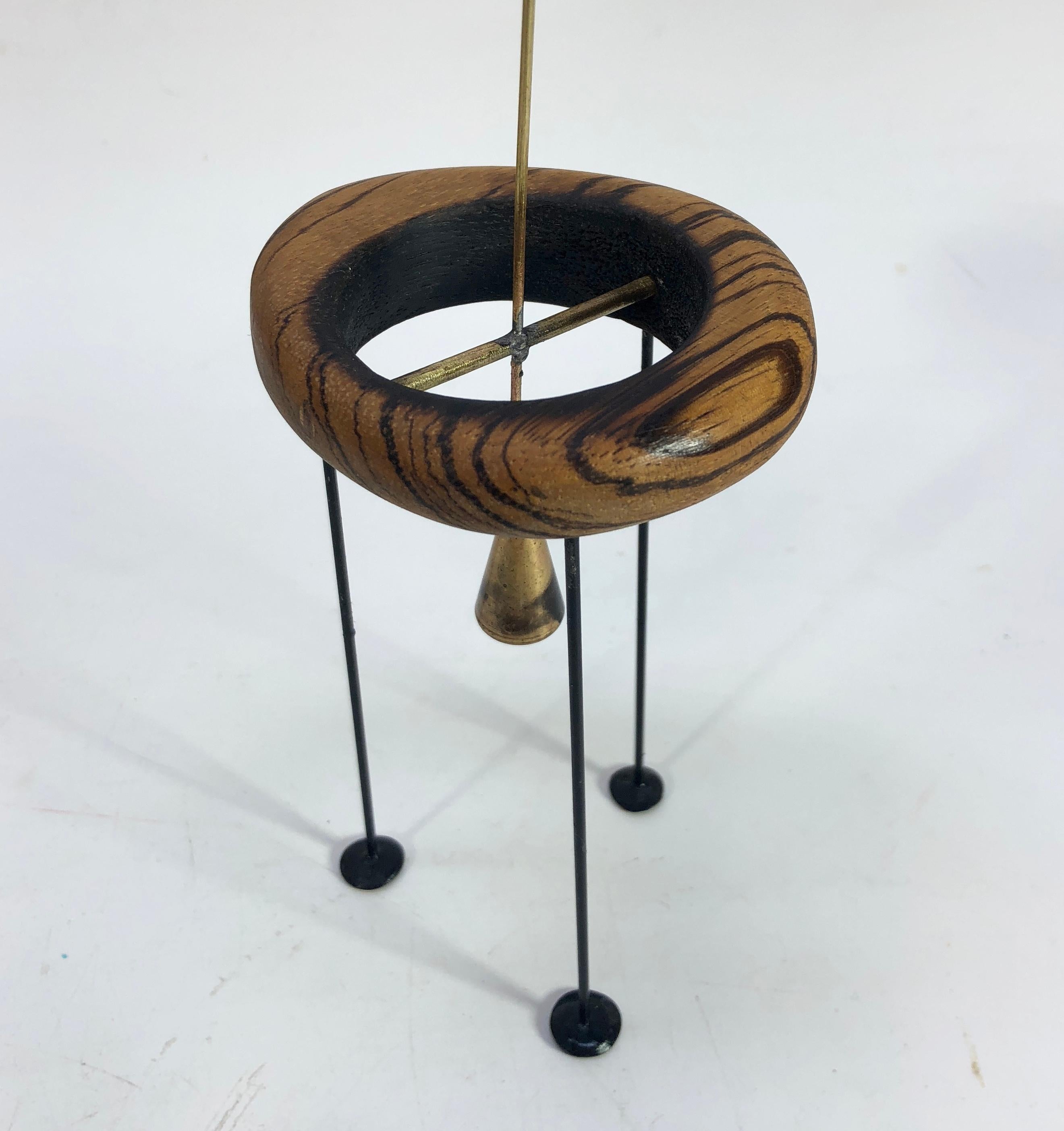 Adam Henderson's The Memory of Time abstract sculpture. A swinging weighted fulcrum suspended in a wood donut and supported by three pod feet.