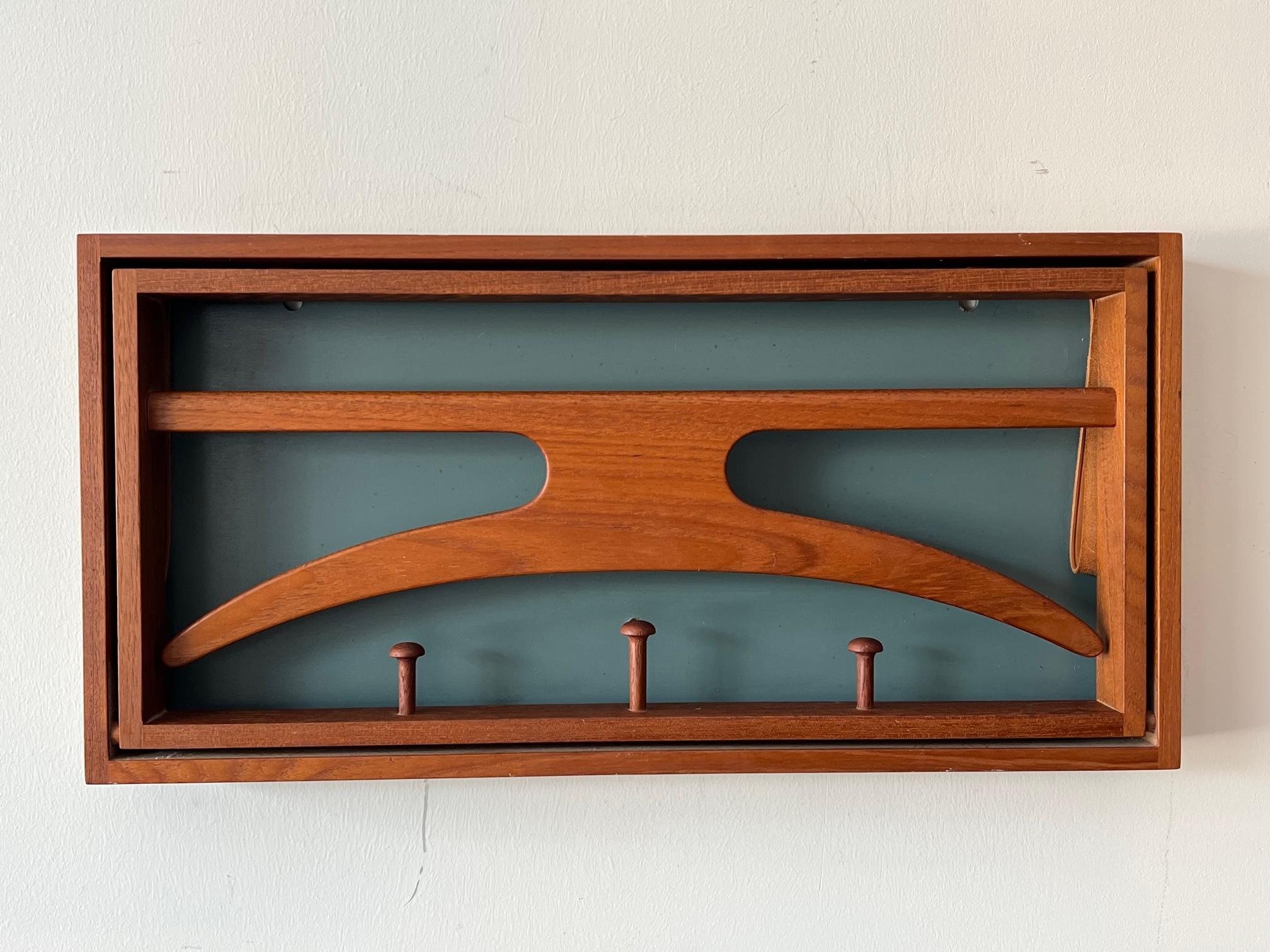 Adam Hoff & Poul Østergaard, Folding Coat Rack, manufactured by Virum Møbelsnedkeri, ca' 1960's.  For wall mounting, this ingenious design features a coat hanger which pulls down, supported with leather straps, giving access to 3 carved pegs behind