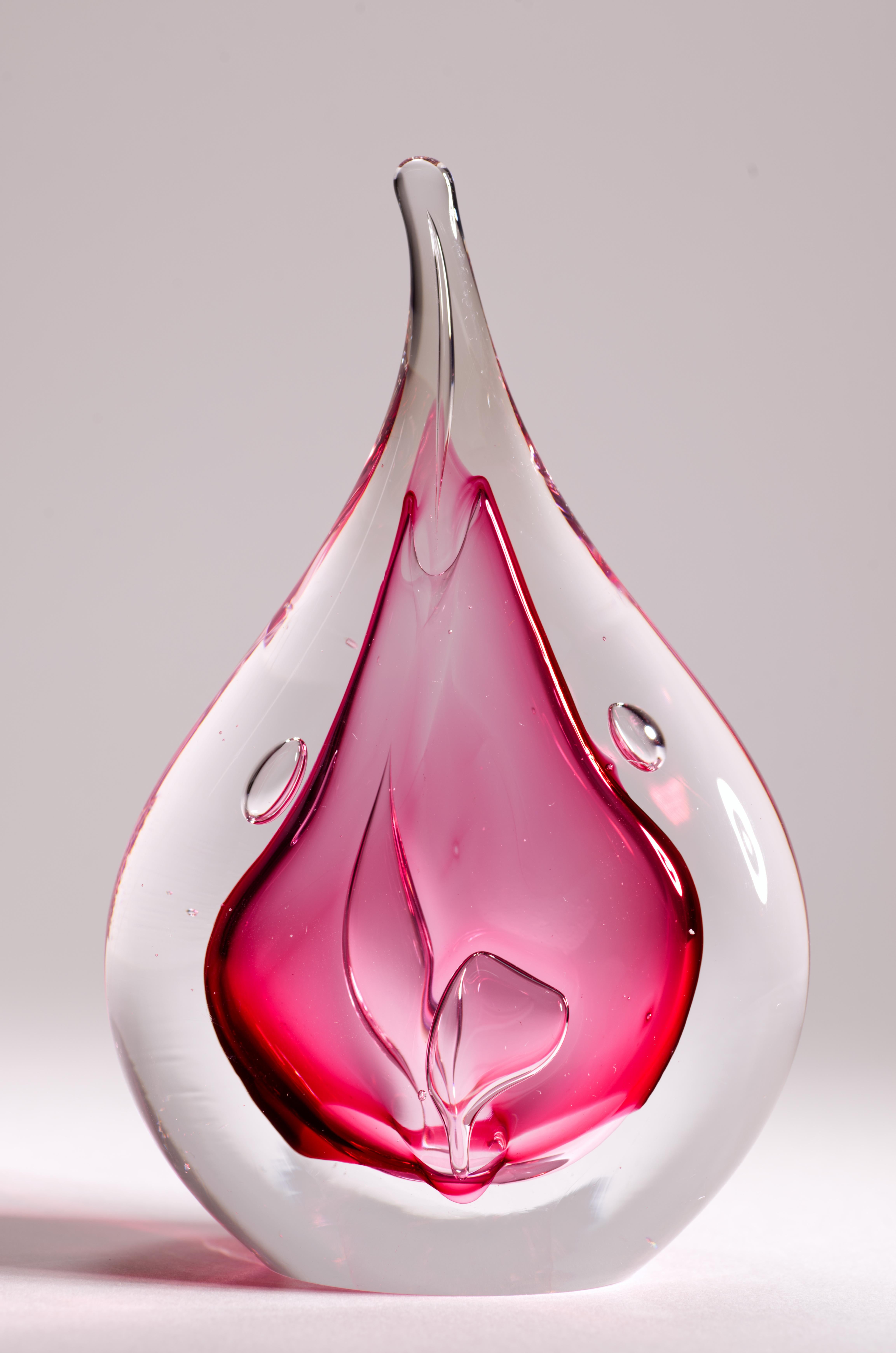  La sculpture en verre d'art abstrait coloré ou presse-papier présente une forme de goutte aplatie avec un noyau central en verre rouge canneberge avec des bulles contrôlées, entouré d'une couche de verre clair selon la technique sommerso.

La pièce