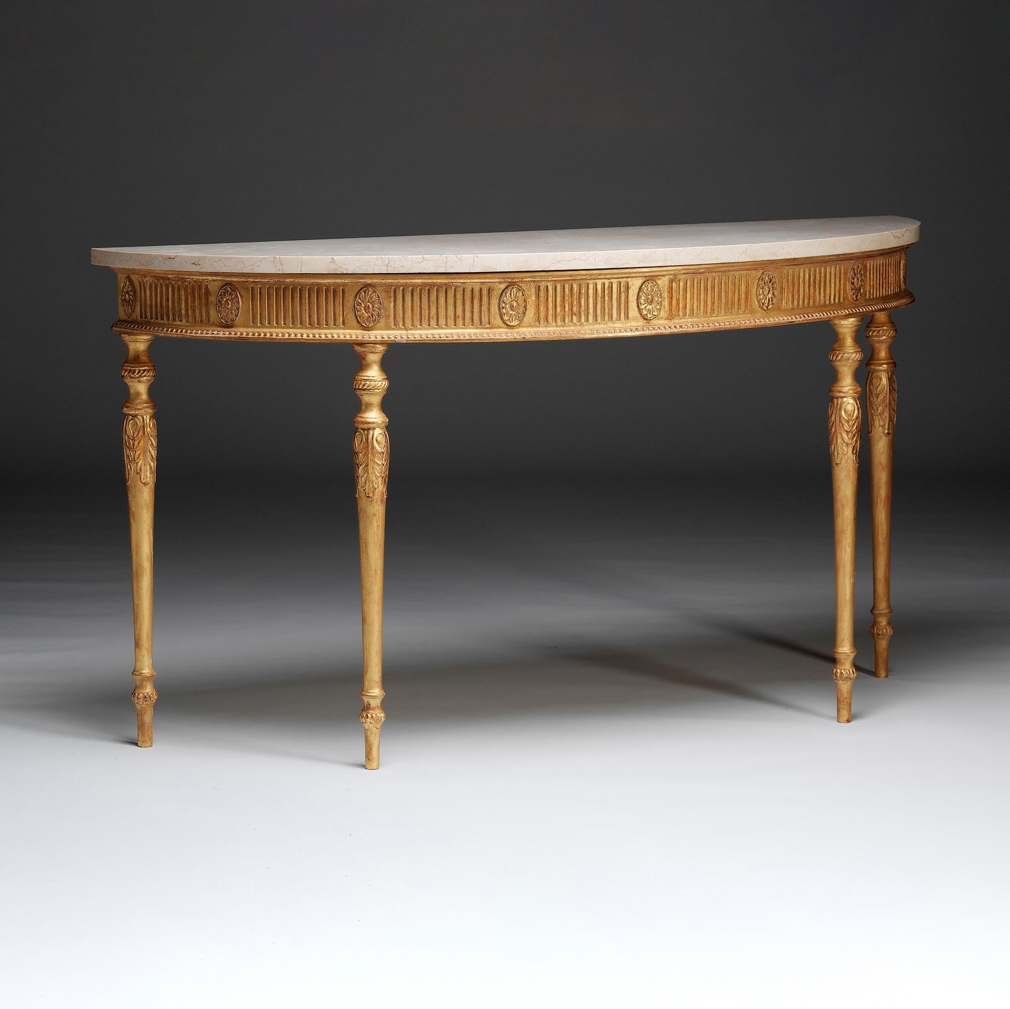 This semi elliptical, gilt-wood marble top side table in the style of George III and the influence of Robert Adam has a fluted frieze punctuated with flower-head paterae between carved mouldings. The turned and tapered legs are capped with acanthus