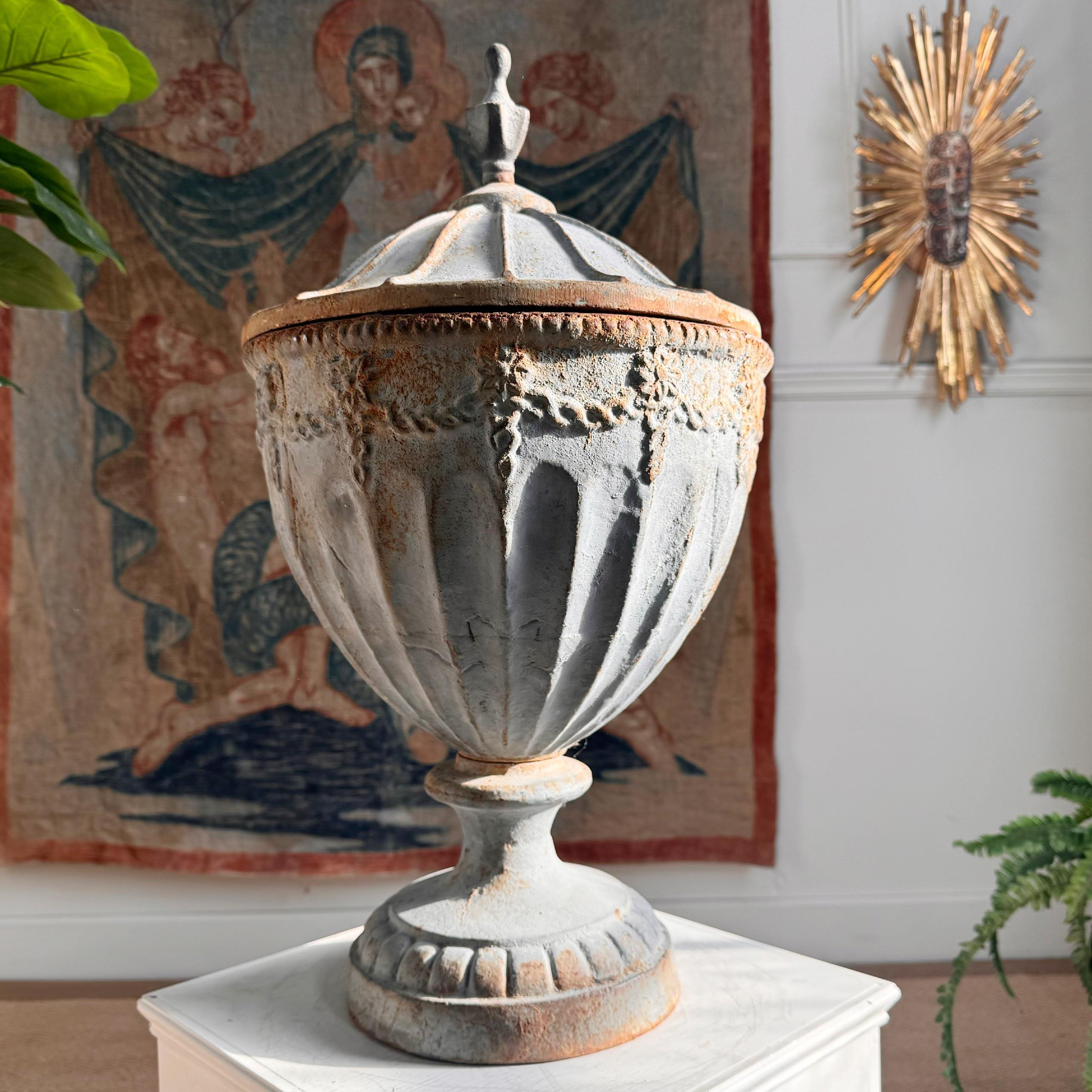 An early 1800’s cast iron urn after the design by Robert Adam, believed to have been forged at the Carron Iron Works, Falkirk. The lidded urn of neoclassical design in a fog blue paint and time worn patina is a wonderful example of its