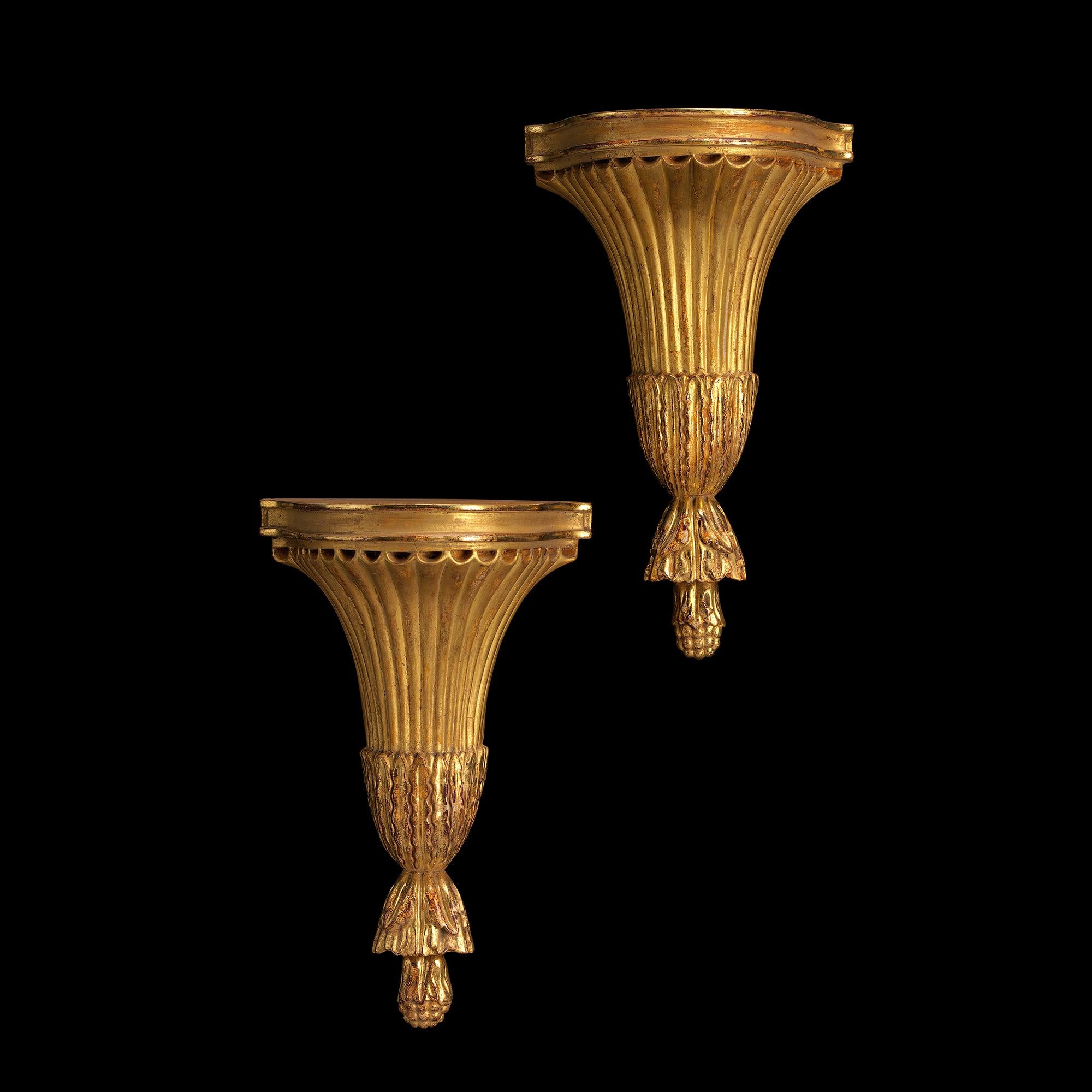 This late 18th century design carved and gilded wood wall bracket has a shaped and double moulded shelf and a tapered fan fluted body. The base is decorated with a lotus leaf collar above a leaf carved and seed pod finial. Available either as a