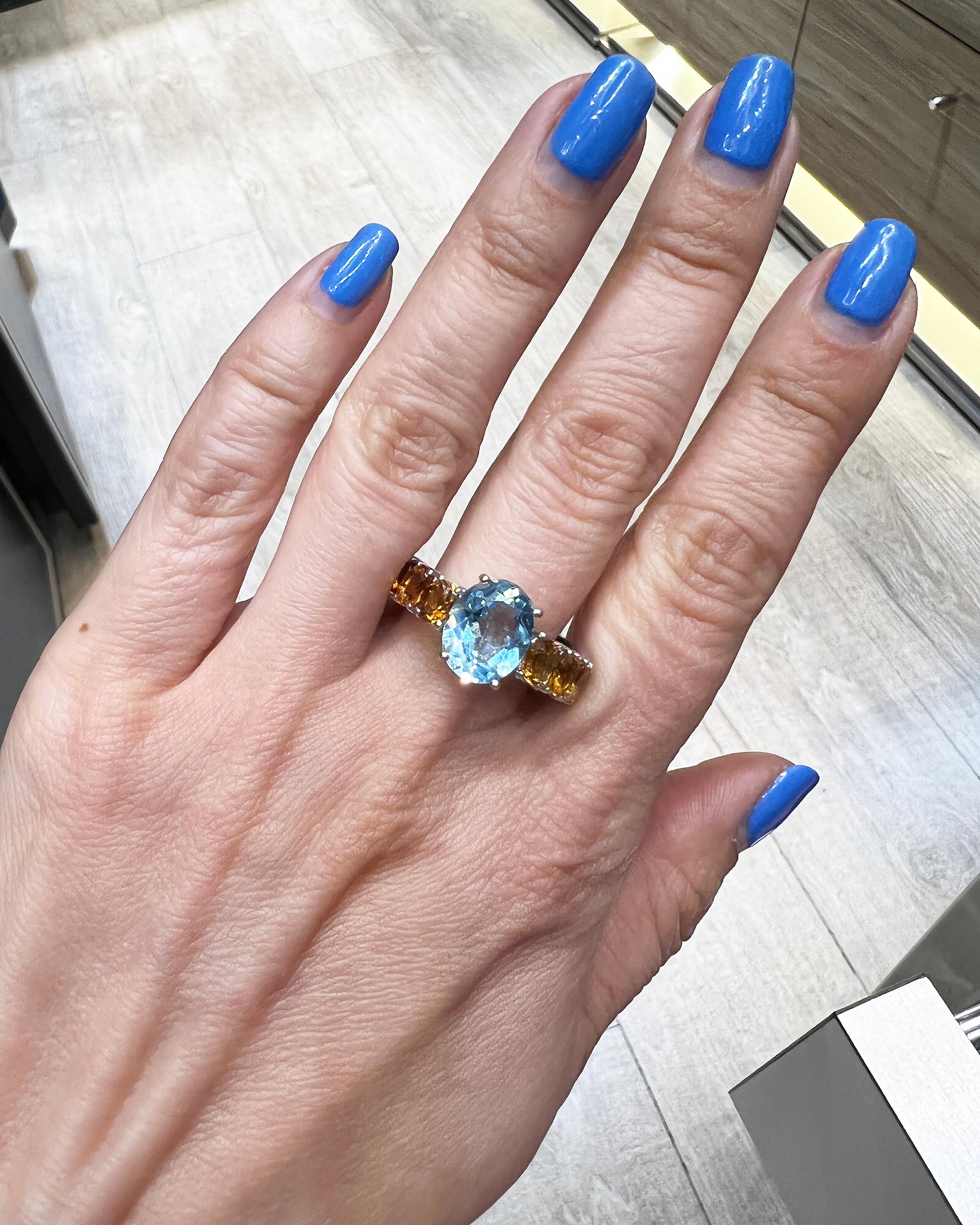 This ring is featuring an oval blue topaz weighing 8.10 carats and and oval citrine stones half-way on both sides of the band.
Metal is 18k white gold.
Weight of the ring is 9.90 grams. 
Size 7.
Retail price is $3,128.
A similar ring available for