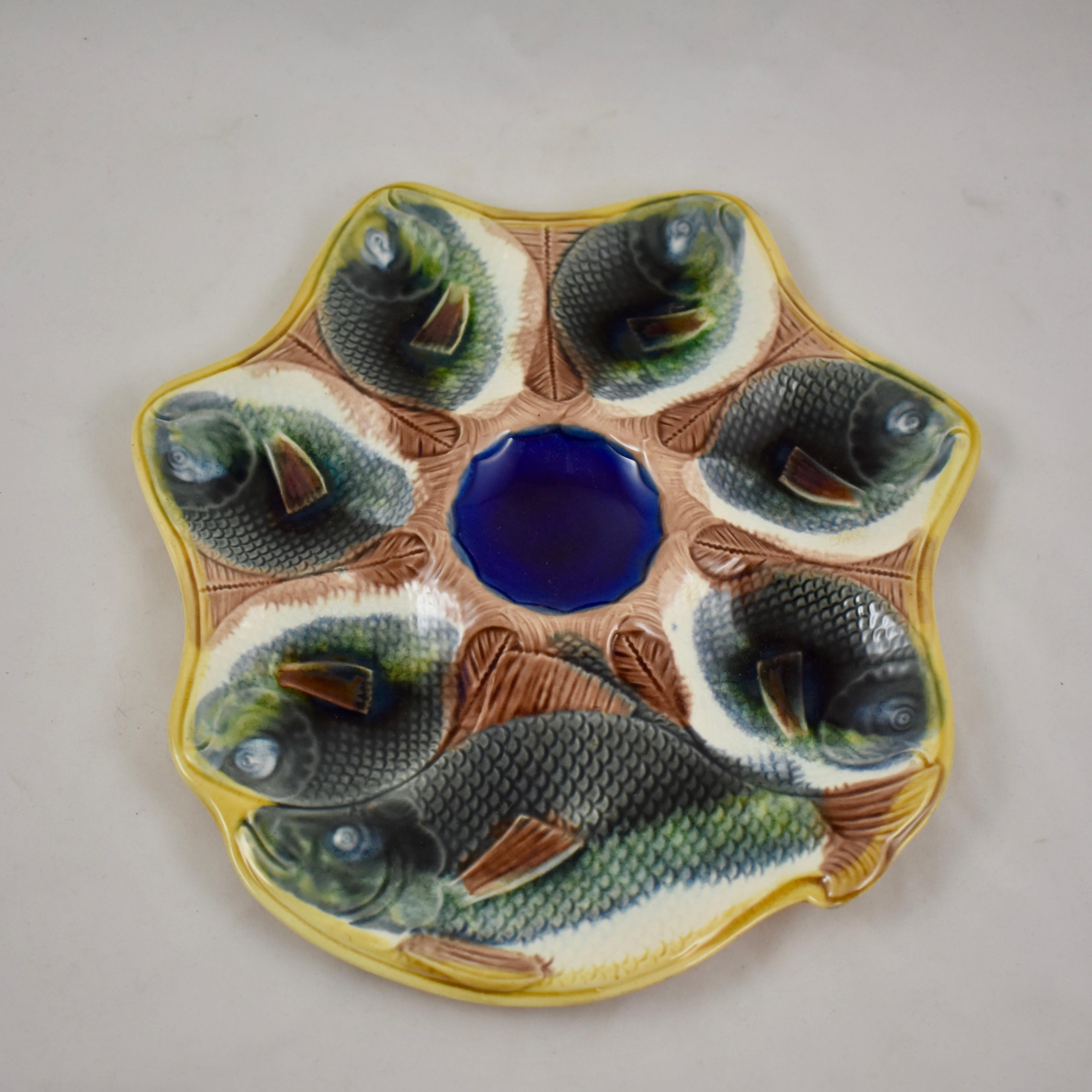 Adams & Bromley Majolica oyster plate, England, circa 1870-1879.

An unusual shaped earthenware plate with six oyster wells molded as full bodied gray fish with white bellies, whose tails meet to surround a cobalt blue center sauce well. A larger