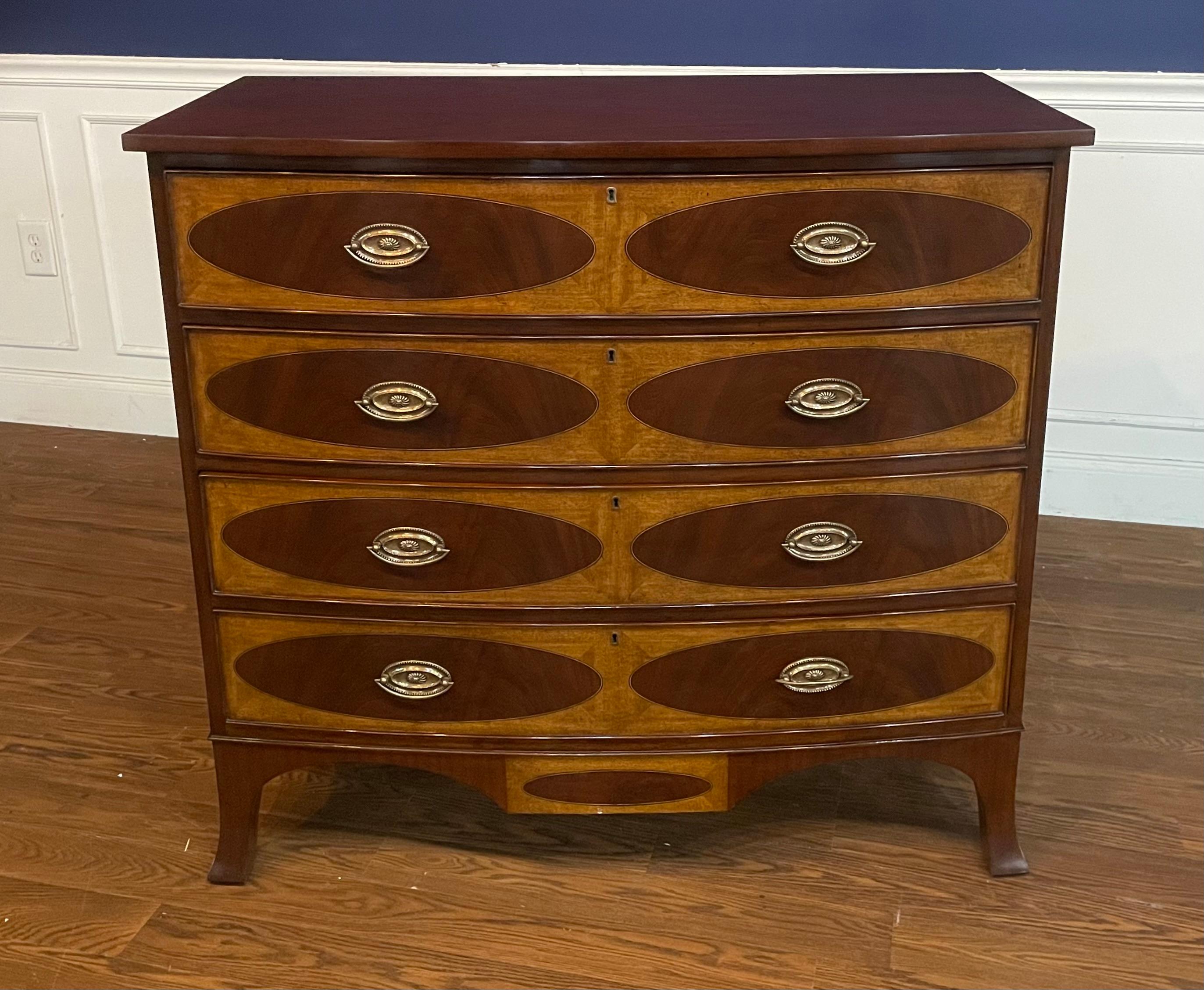 This is a classic inlaid bow front chest by Leighton Hall. Its design was inspired by Adams style chests from the early 1800s. It features four drawers, solid brass hardware and faux key holes. The drawer fronts have swirly crotch mahogany oval