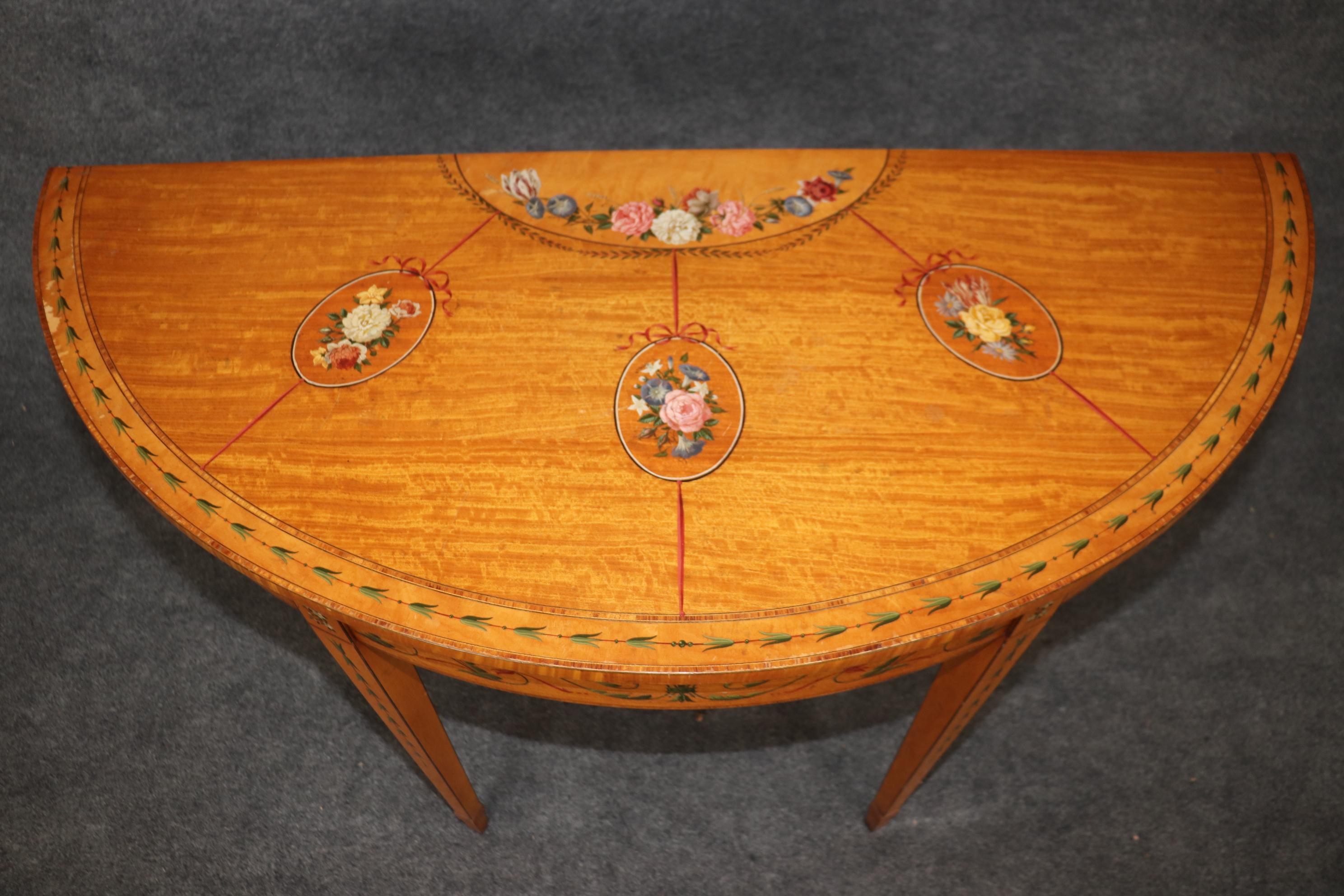 This is a beautiful hand-painted English 1920s era satinwood Adams demilune console. The table is beautifully made with the finest satinwood and amazing figuring and sumptuous hand-painted flowers and garlands. The table is in good condition with