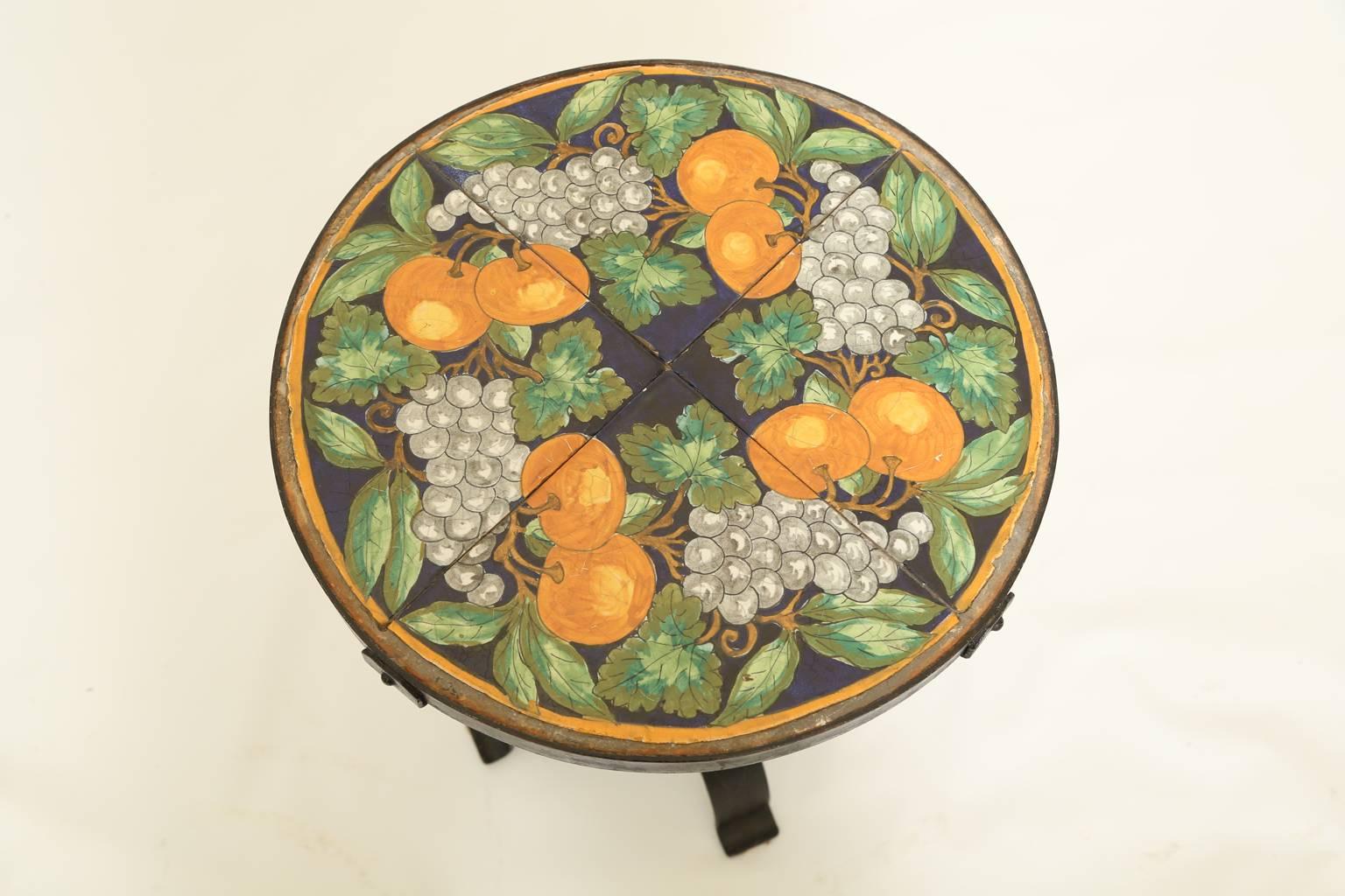 Side table, attributed to renowned Florida architect, Addison Mizner, having a round top of hand-painted pottery tiles, on custom iron base, corner straps mount the top to its pedestal, with a central decoration, raised on four, splayed legs, ending