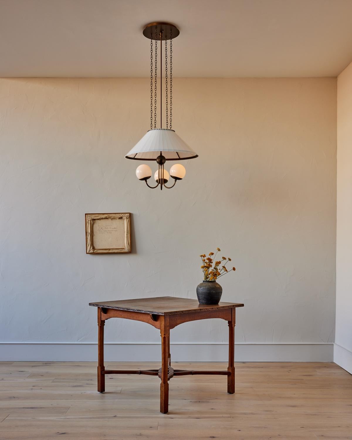 Il lampadario Adele in vetro lattiginoso è caratterizzato da sfere in vetro lattiginoso sospese sotto un paralume in vetro lattiginoso per una luce nitida e pulita. I dettagli in ottone antico e i bracci in ottone strofinato a olio conferiscono un