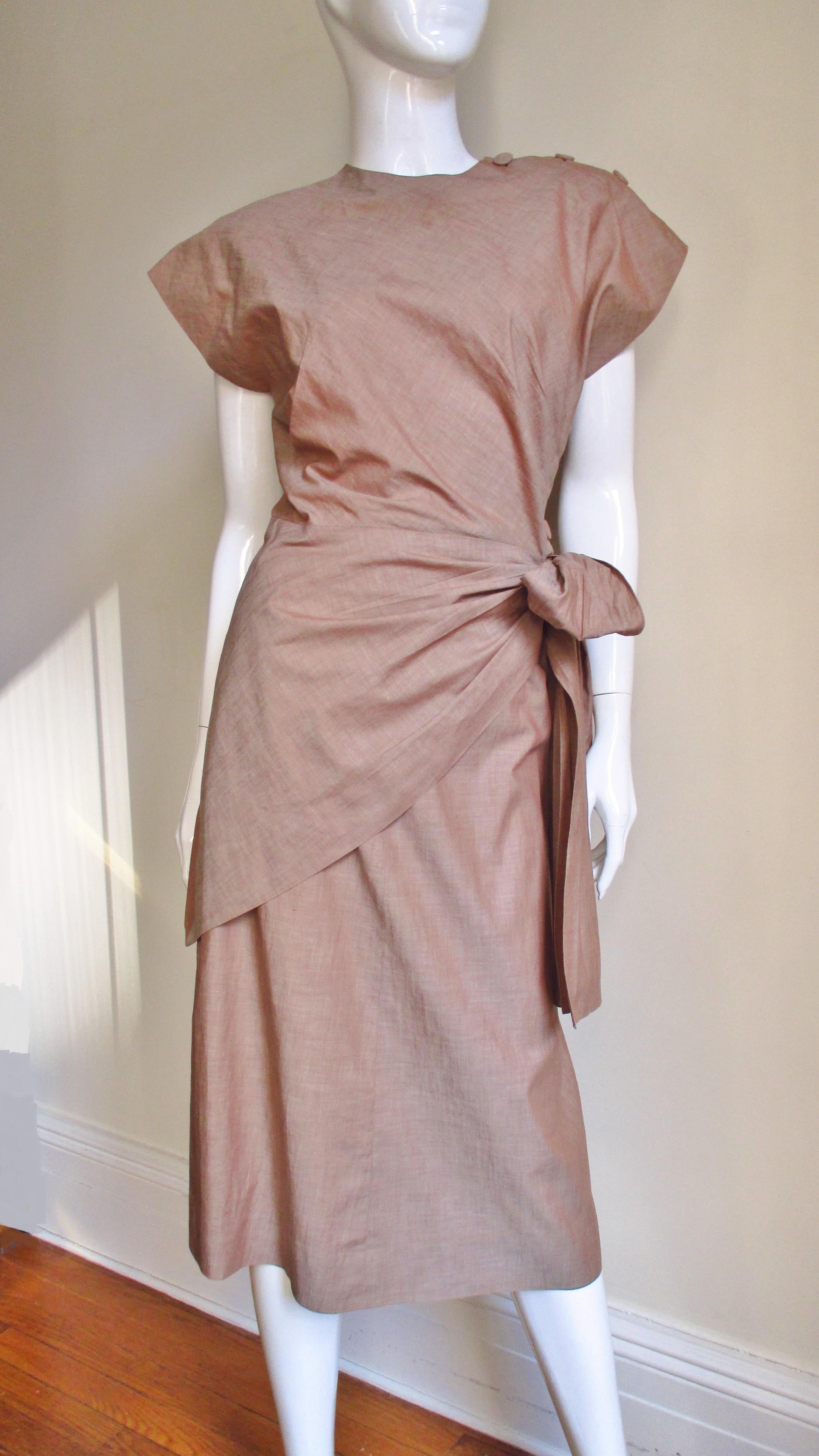 A fabulous 2 piece skirt and top set in a tan cotton linen blend.  The top has a crew neck, cap sleeves, shoulder pads and wraps closing at one side and shoulder with self covered buttons and bound buttonholes plus ties at that waist. The A line